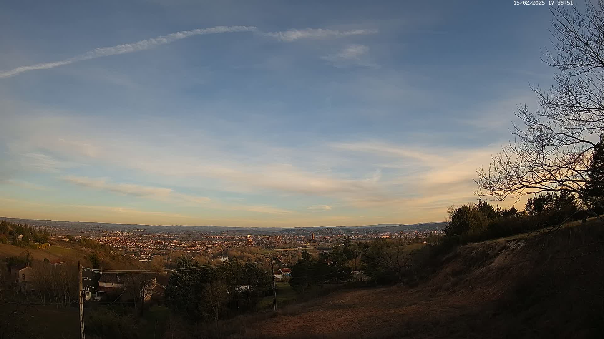 A panoramic view of a city sprawling across a valley beneath a partly cloudy twilight sky.