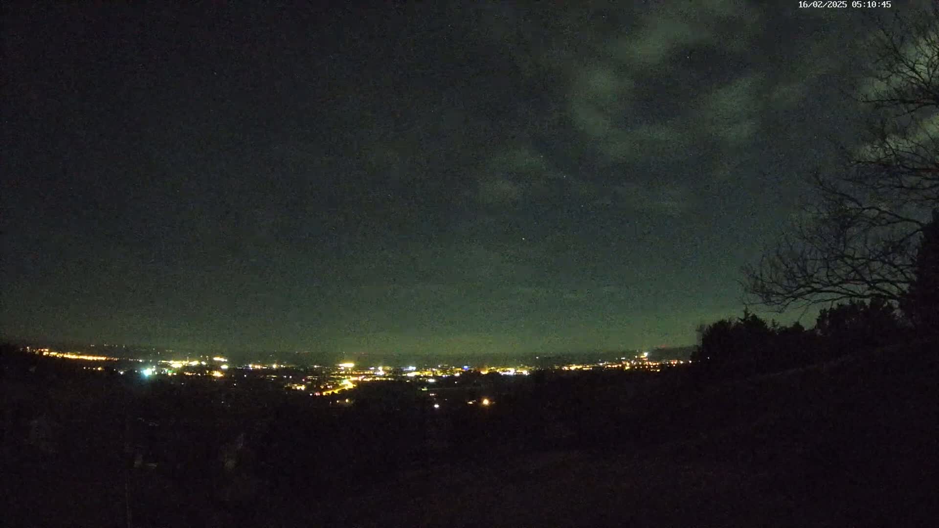 A nighttime view of a distant city's lights under a partly cloudy sky.