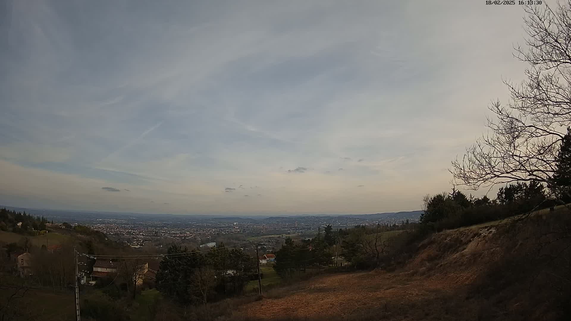 A view from a hillside shows a distant city under a mostly cloudy sky.