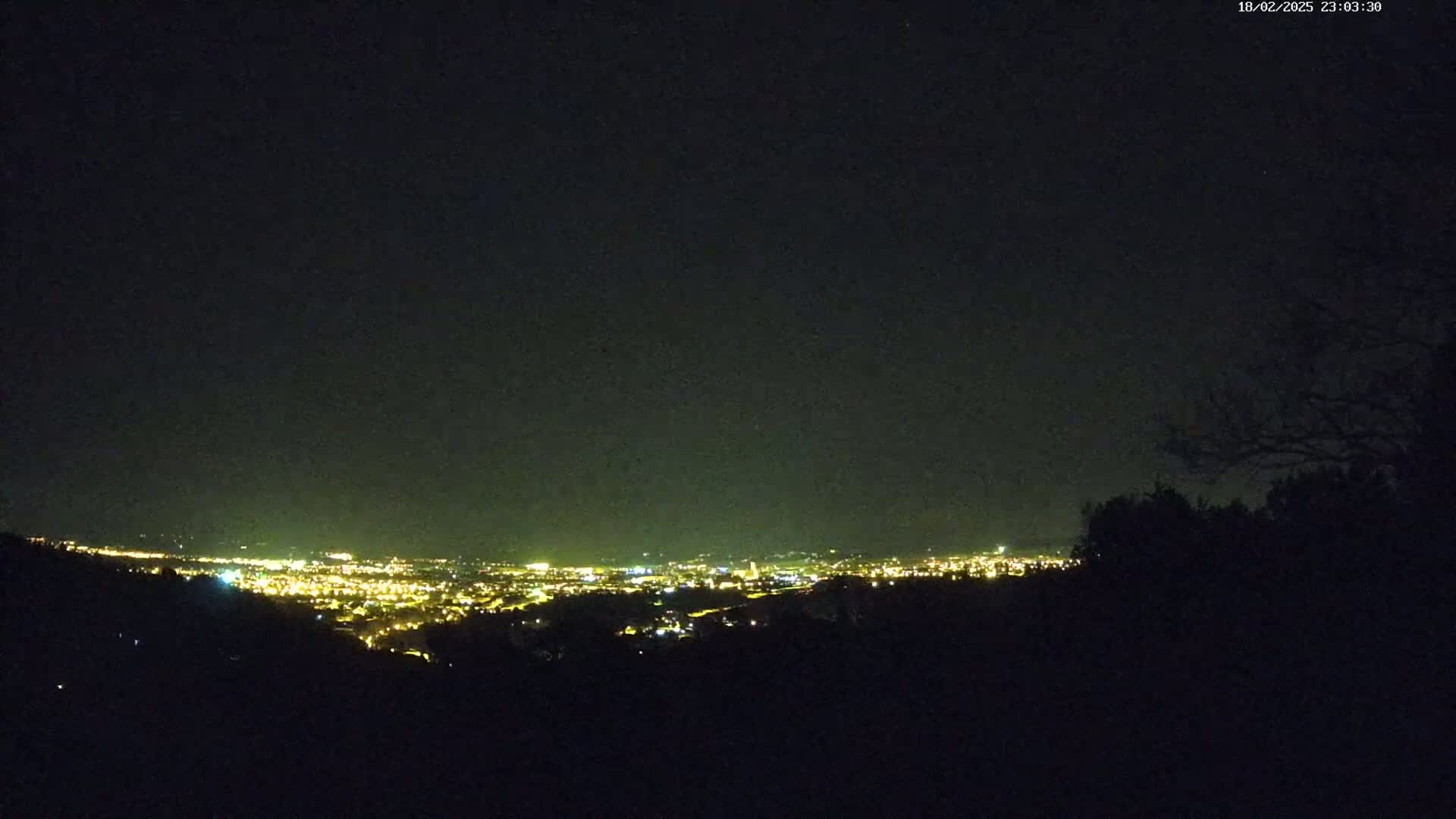 A nighttime view from a hilltop shows a sprawling city glowing with lights under a dark, clear sky.