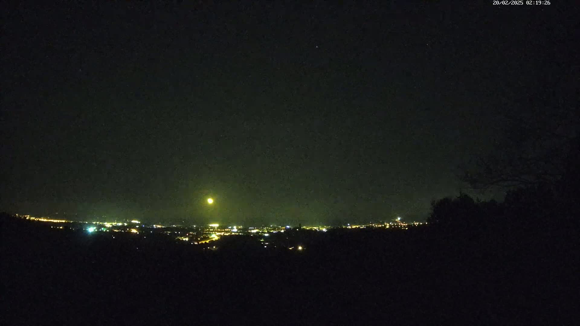 A bright moon illuminates a distant city skyline at night.