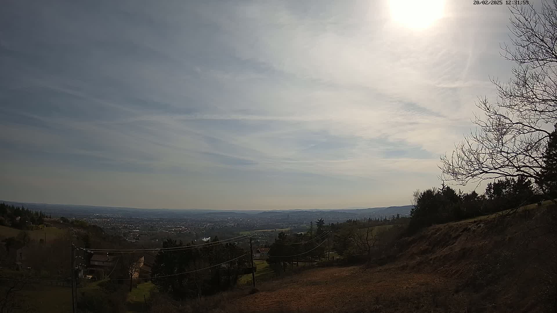 A hilly landscape with a distant city view under a partly cloudy sky with bright sunshine.