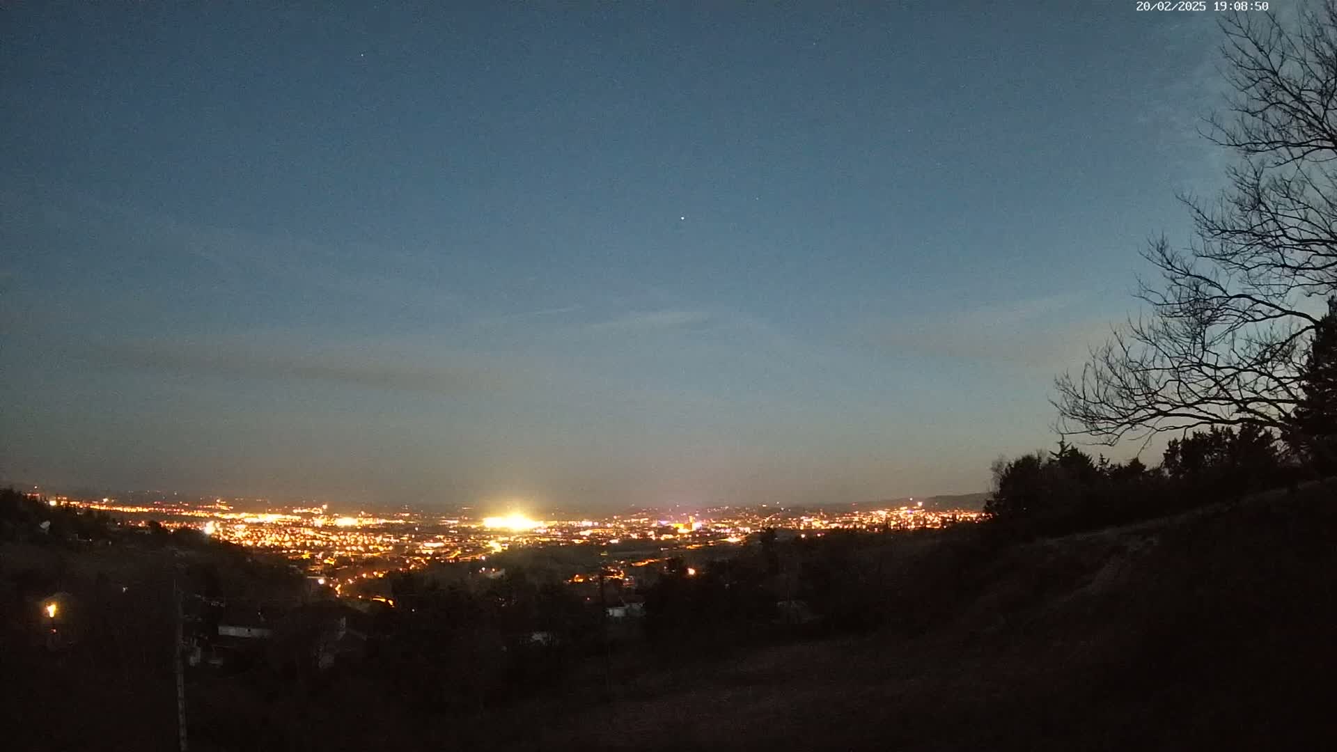 A nighttime view from a hill overlooking a brightly lit city under a clear, dark blue sky.