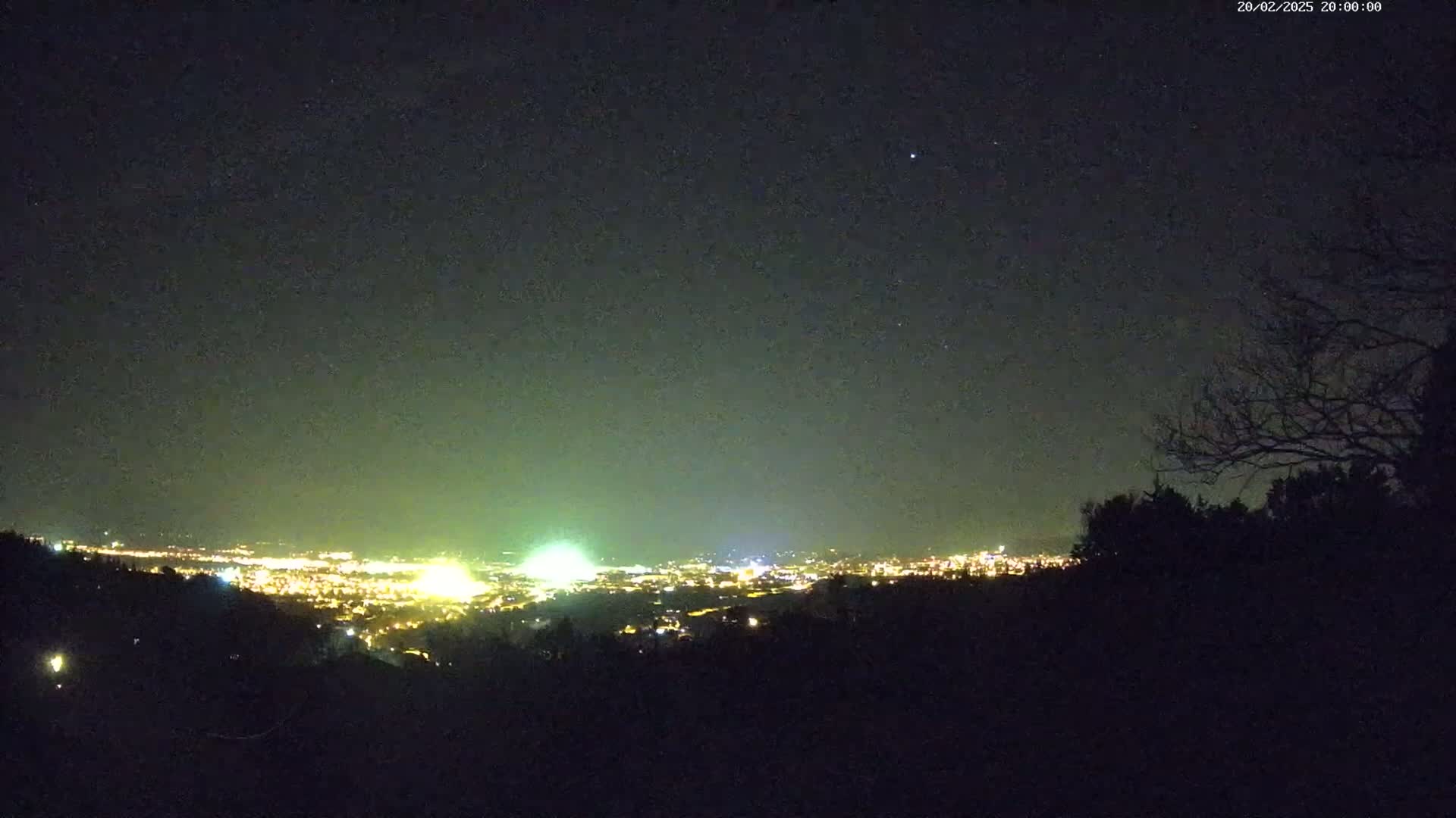 A nighttime view shows a distant city illuminated with lights under a mostly clear, dark sky.