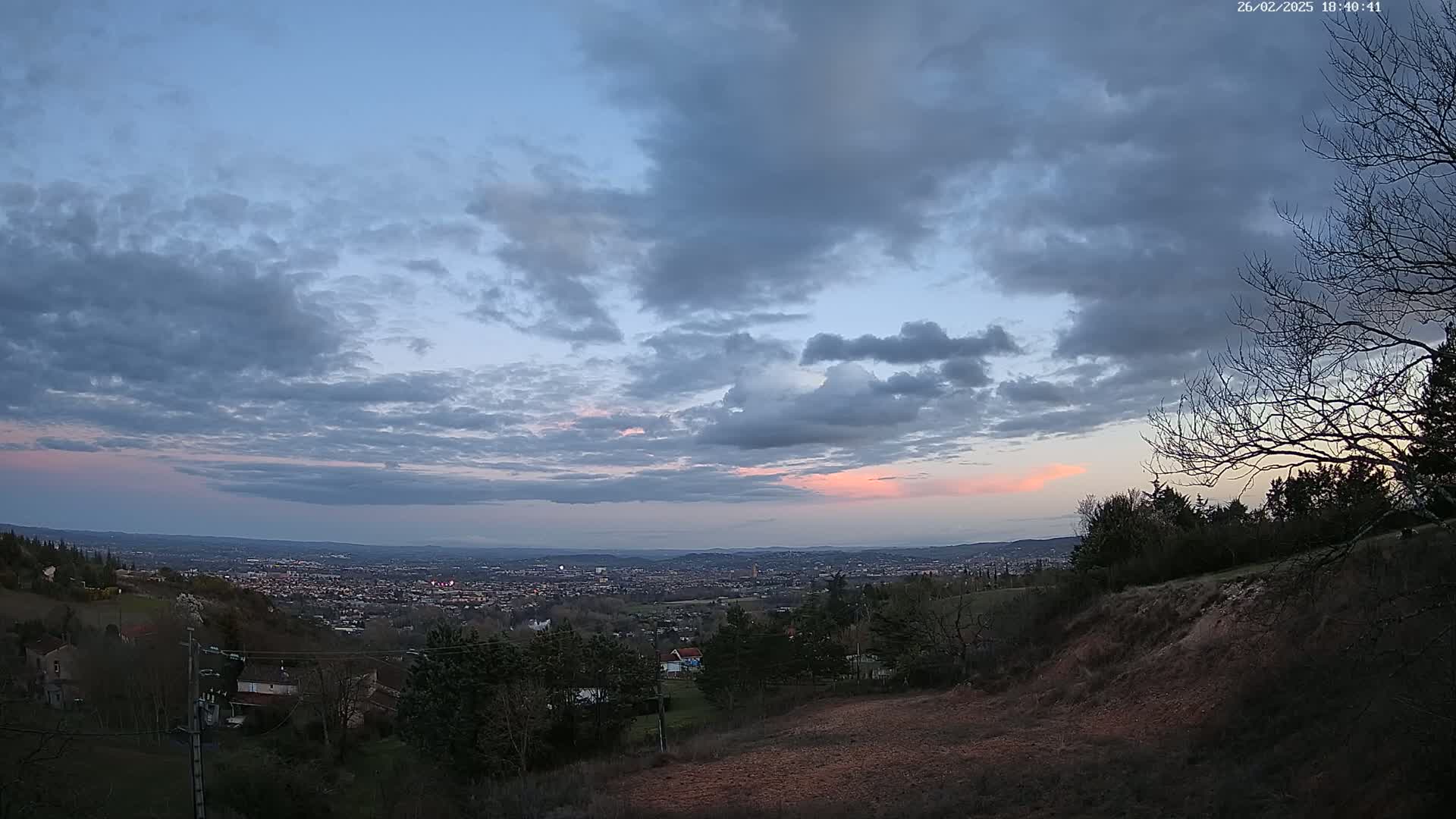 A partly cloudy twilight sky over a sprawling town nestled in a valley, viewed from a hilltop.