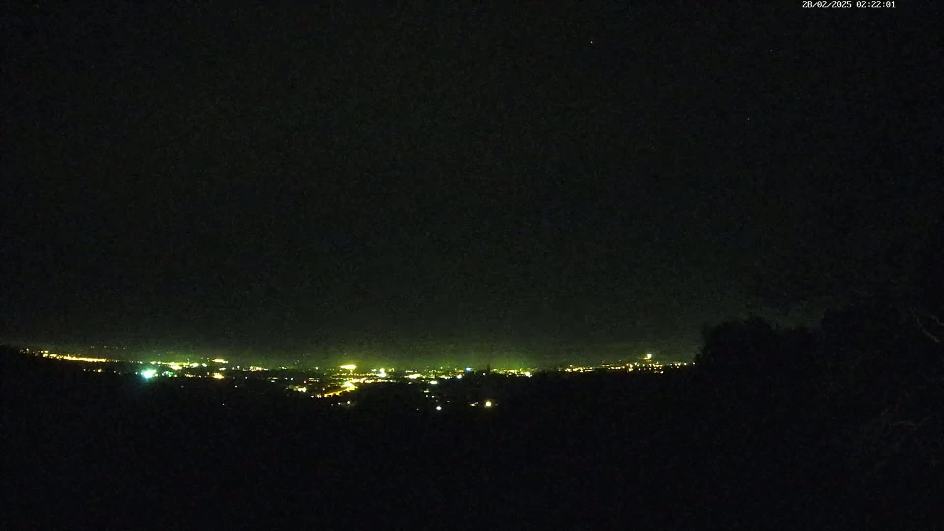 A nighttime view of a distant city skyline illuminated by lights under a dark, clear sky.