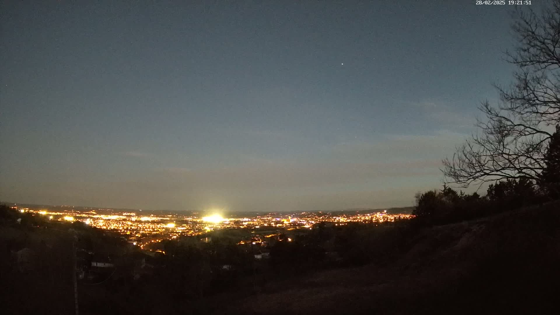 A nighttime view from an elevated position shows a distant city illuminated with lights under a twilight sky.