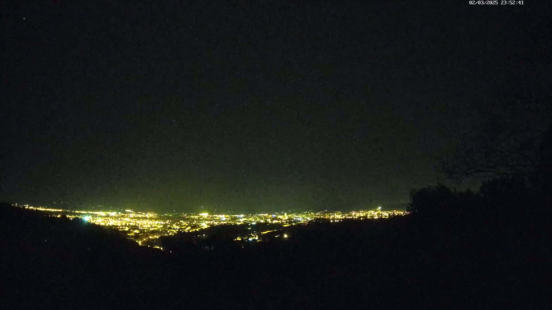 A nighttime view from a hilltop overlooking a distant city illuminated by many lights under a clear, dark sky.