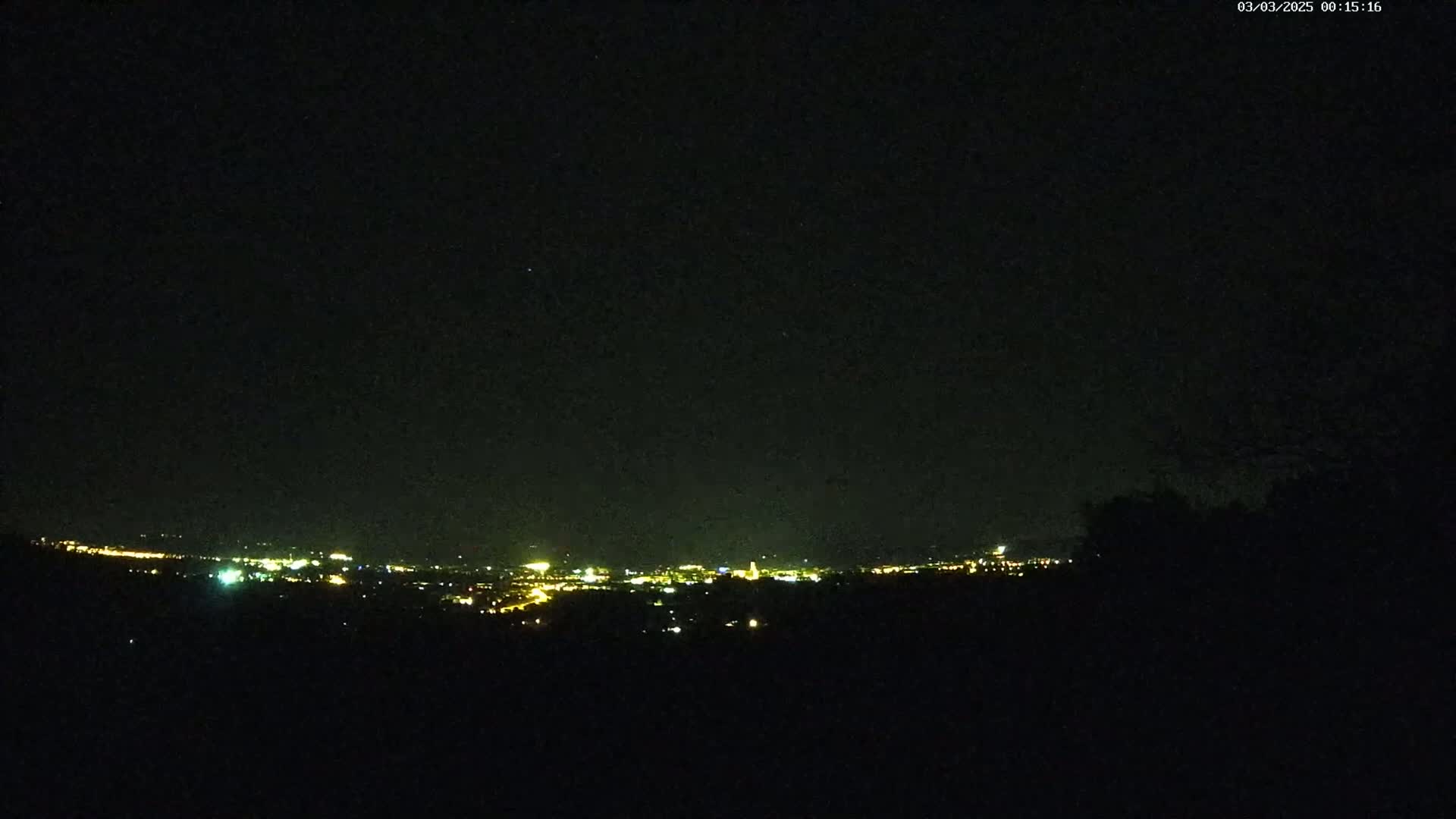 A nighttime long shot shows a distant city glowing with lights under a clear, dark sky.