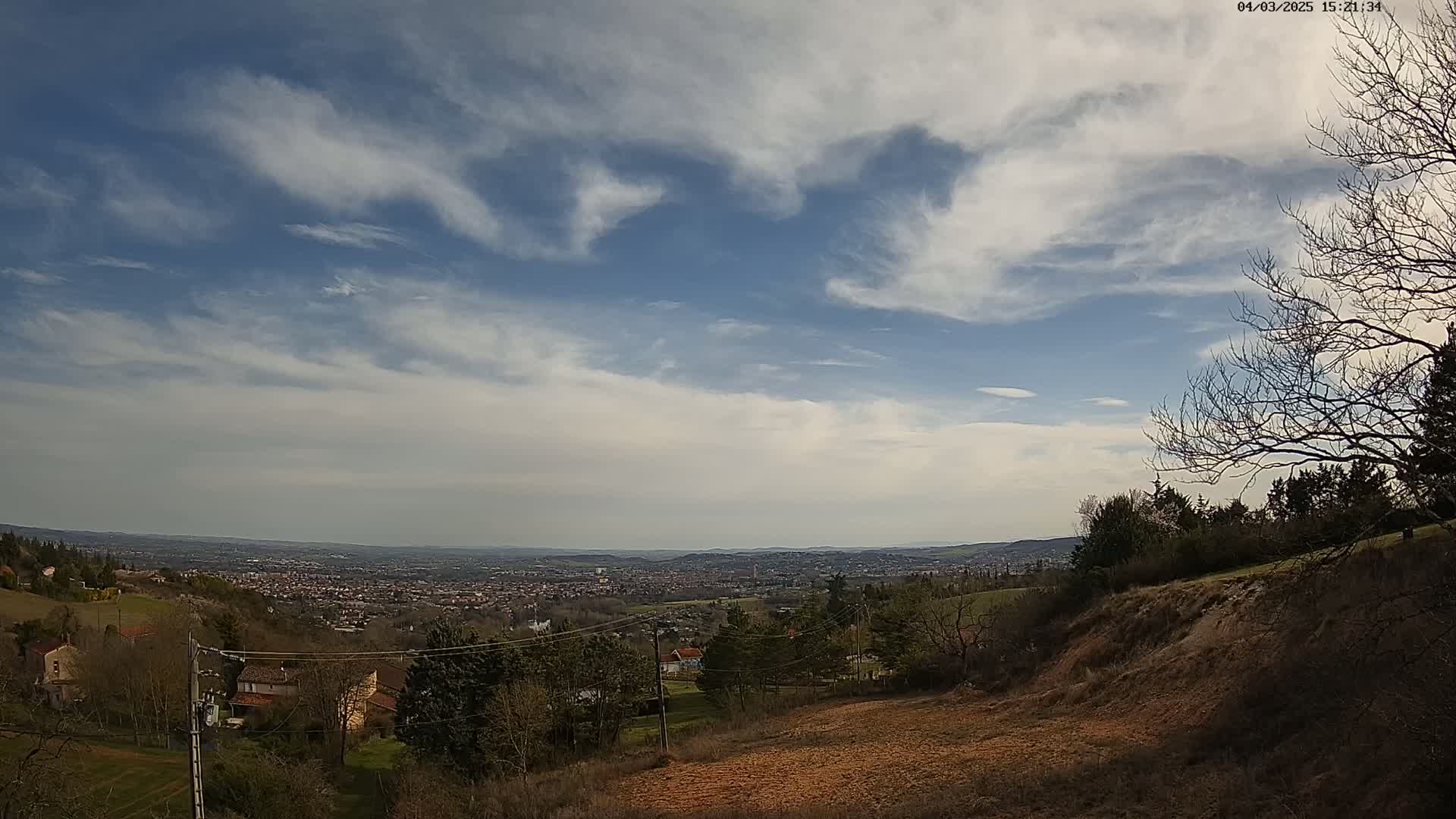 A partly cloudy sky overlooks a sprawling valley town, hills, and sparsely wooded areas.