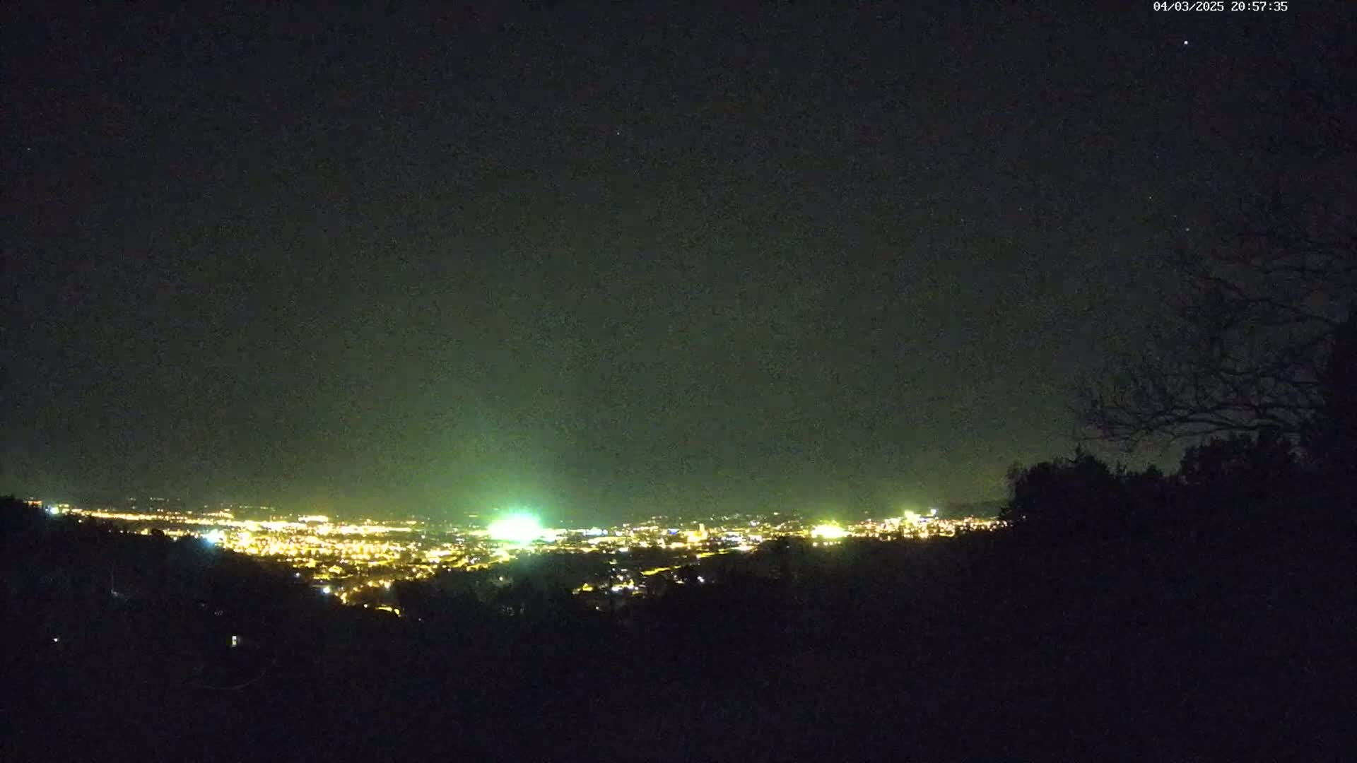 A nighttime view from an elevated position shows a city's lights spread across a valley under a clear, dark sky.