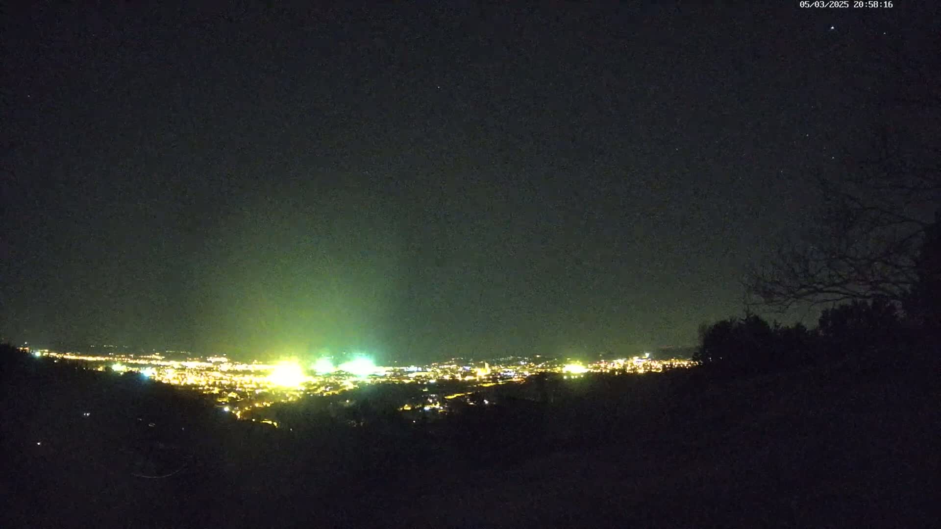 A nighttime view from a hilltop shows a distant city glowing with lights under a clear, dark sky.
