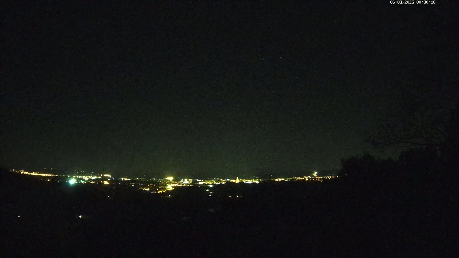 A nighttime view shows a distant city glowing with lights under a clear, starry sky.