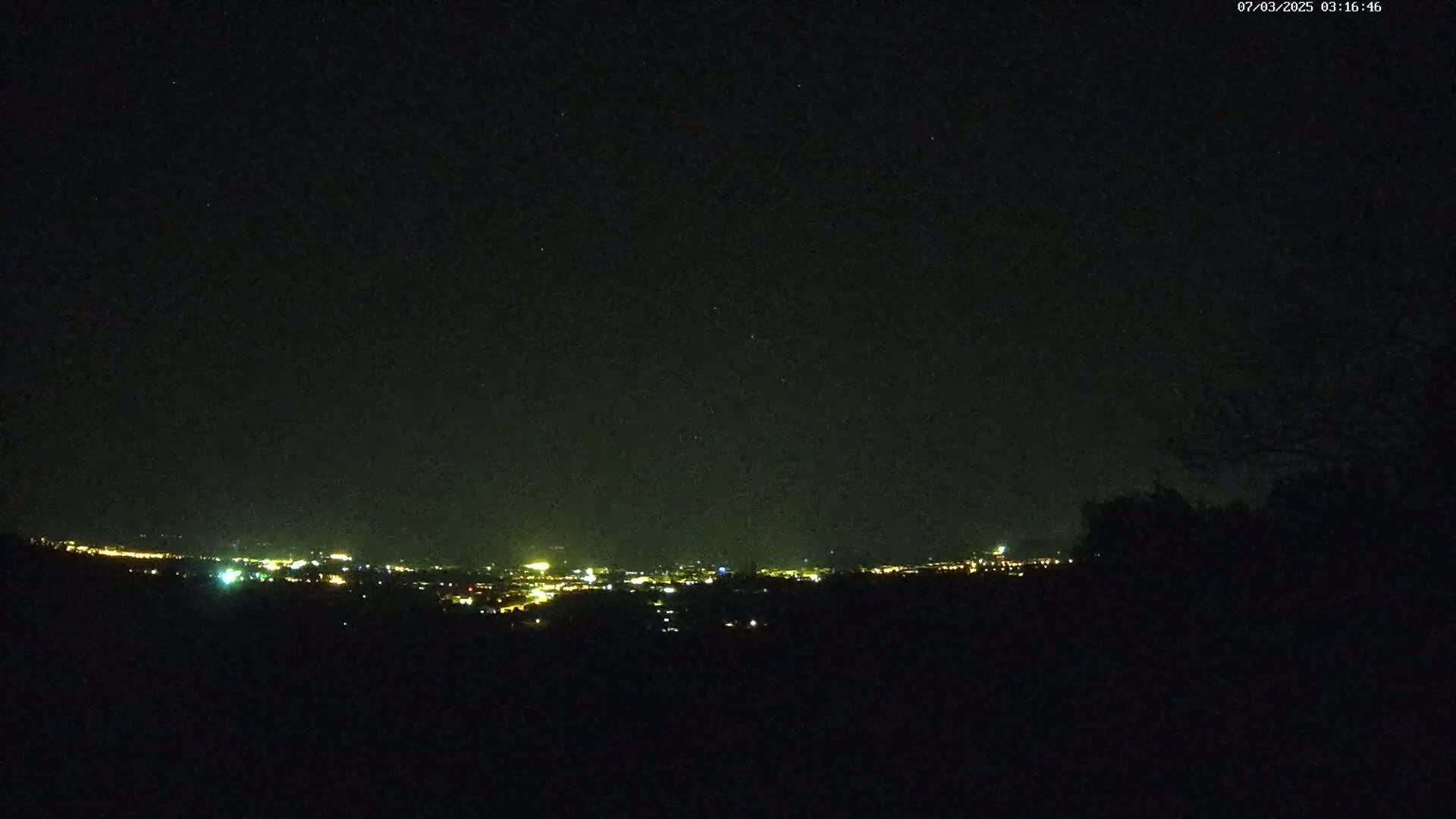 A nighttime view of a distant city's lights spread across a dark horizon under a clear, starlit sky.