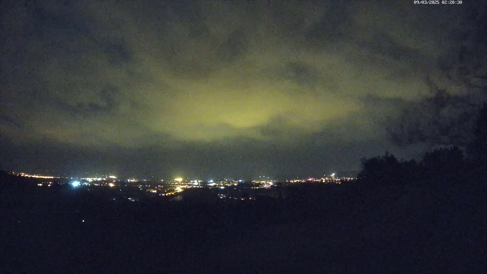 A nighttime view of a city skyline dimly lit under a cloudy, yellowish sky.