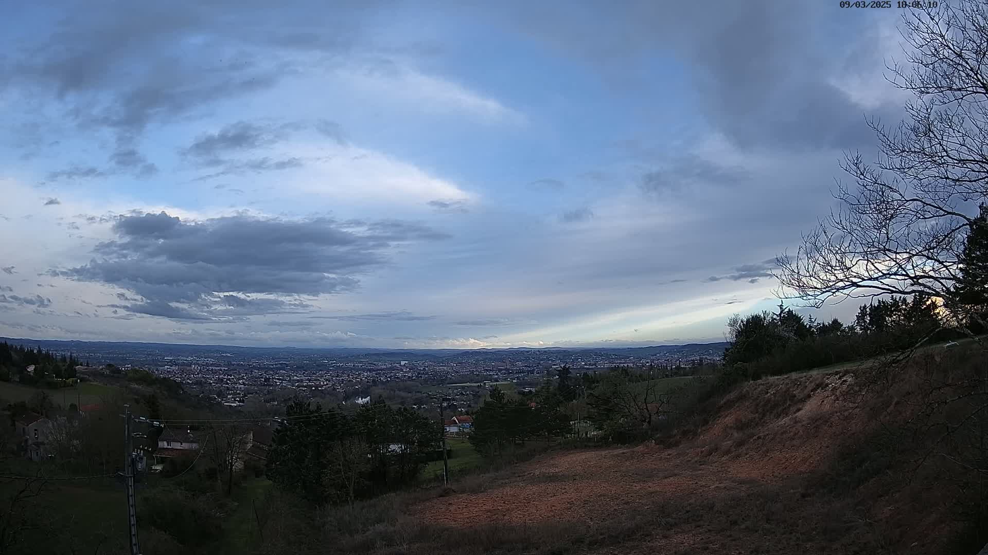 A hilly landscape under a partly cloudy sky overlooks a sprawling city in the distance.