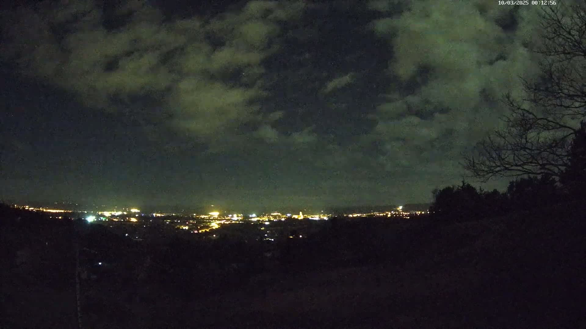 A nighttime view of a city skyline speckled with lights beneath a cloudy sky.