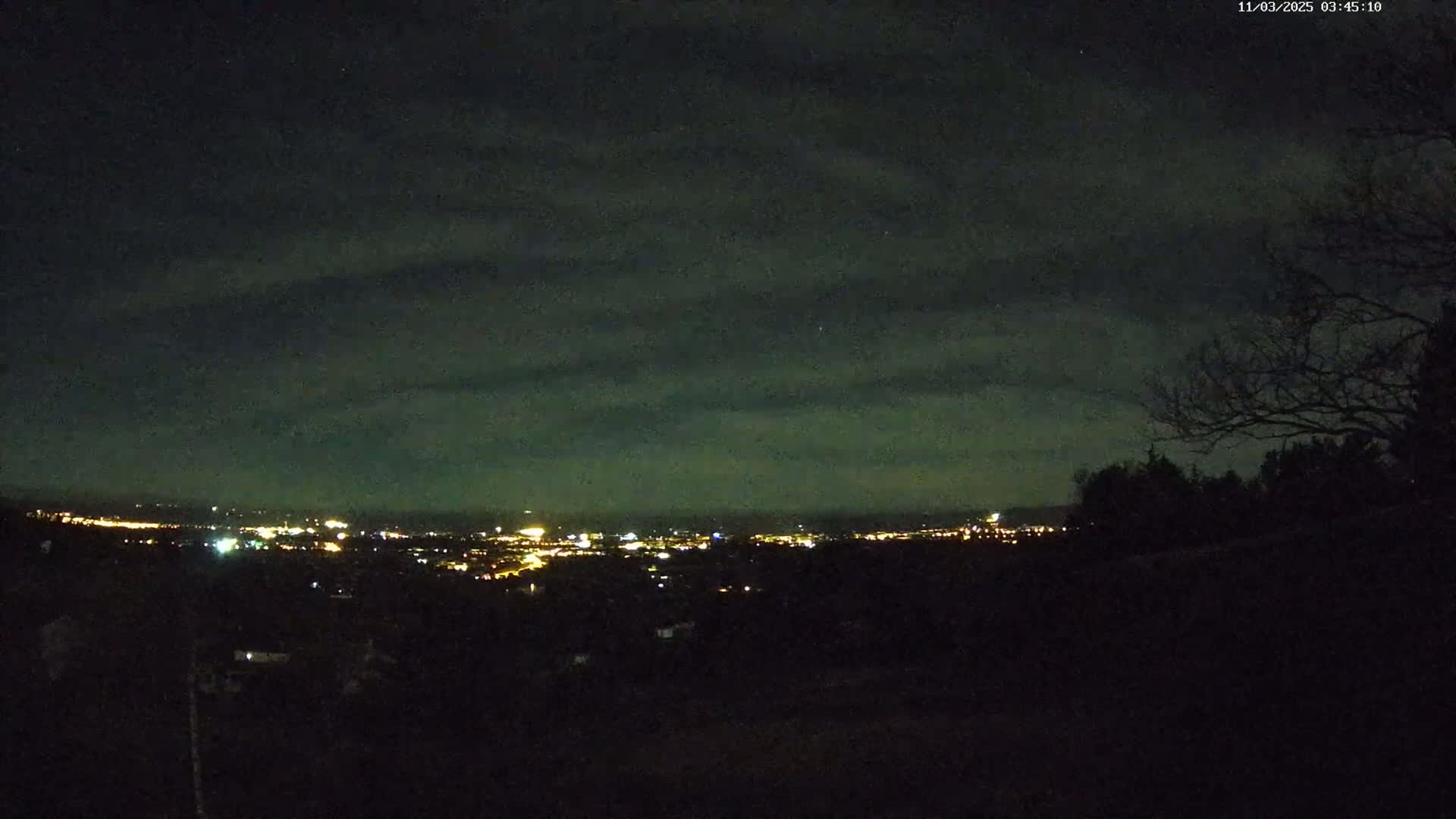 A nighttime view of a distant city illuminated with lights under a cloudy sky.