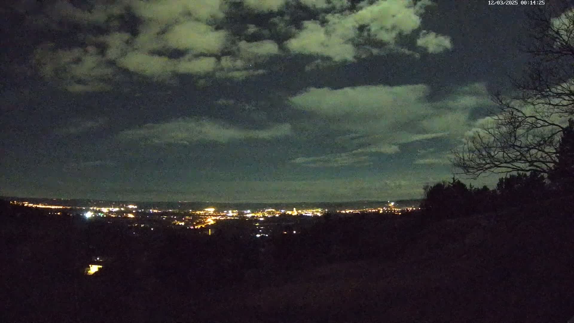 A nighttime view of a city skyline illuminated by lights under a cloudy sky.
