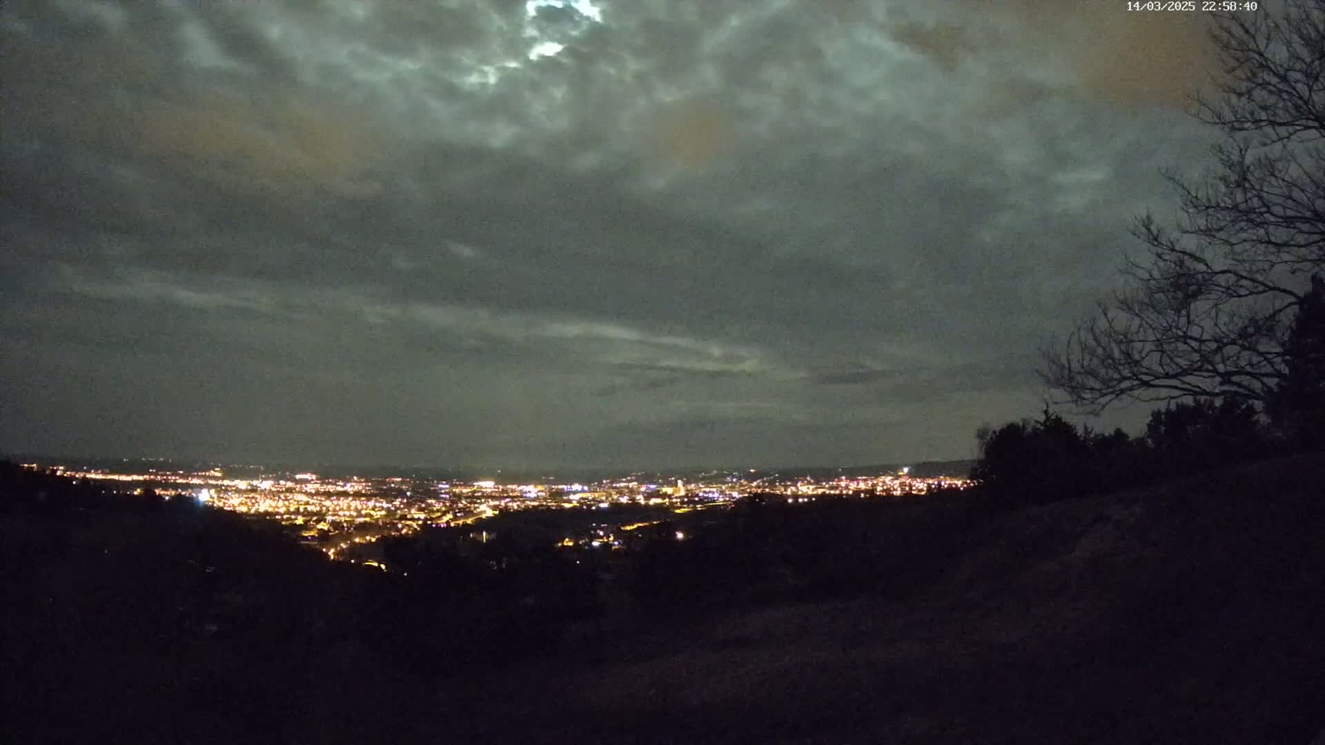 A nighttime view of a city illuminated below a mostly cloudy sky.