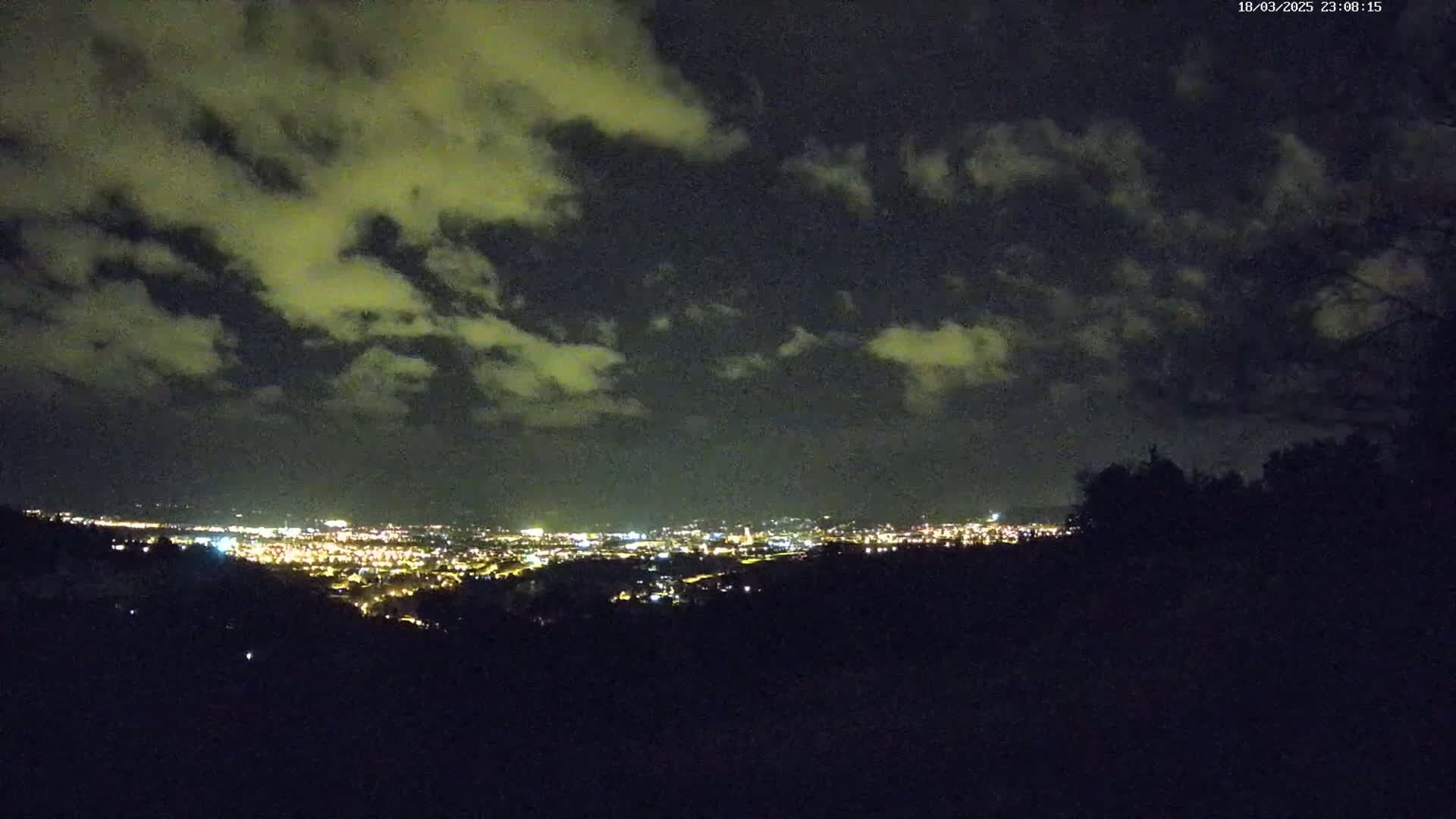 A nighttime view of a city illuminated by lights below a cloudy sky.