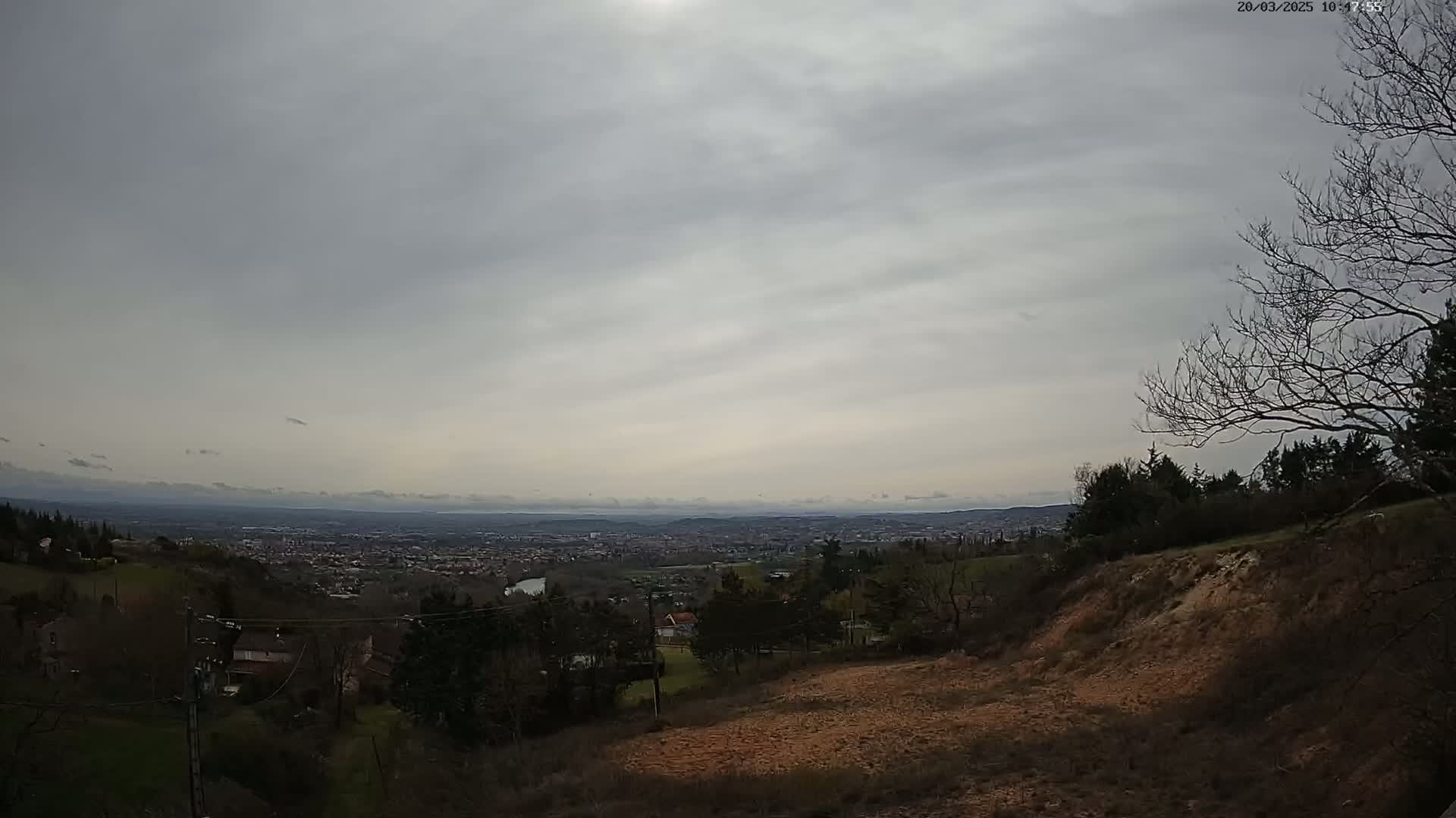 A hillside overlooking a distant city under a cloudy sky.