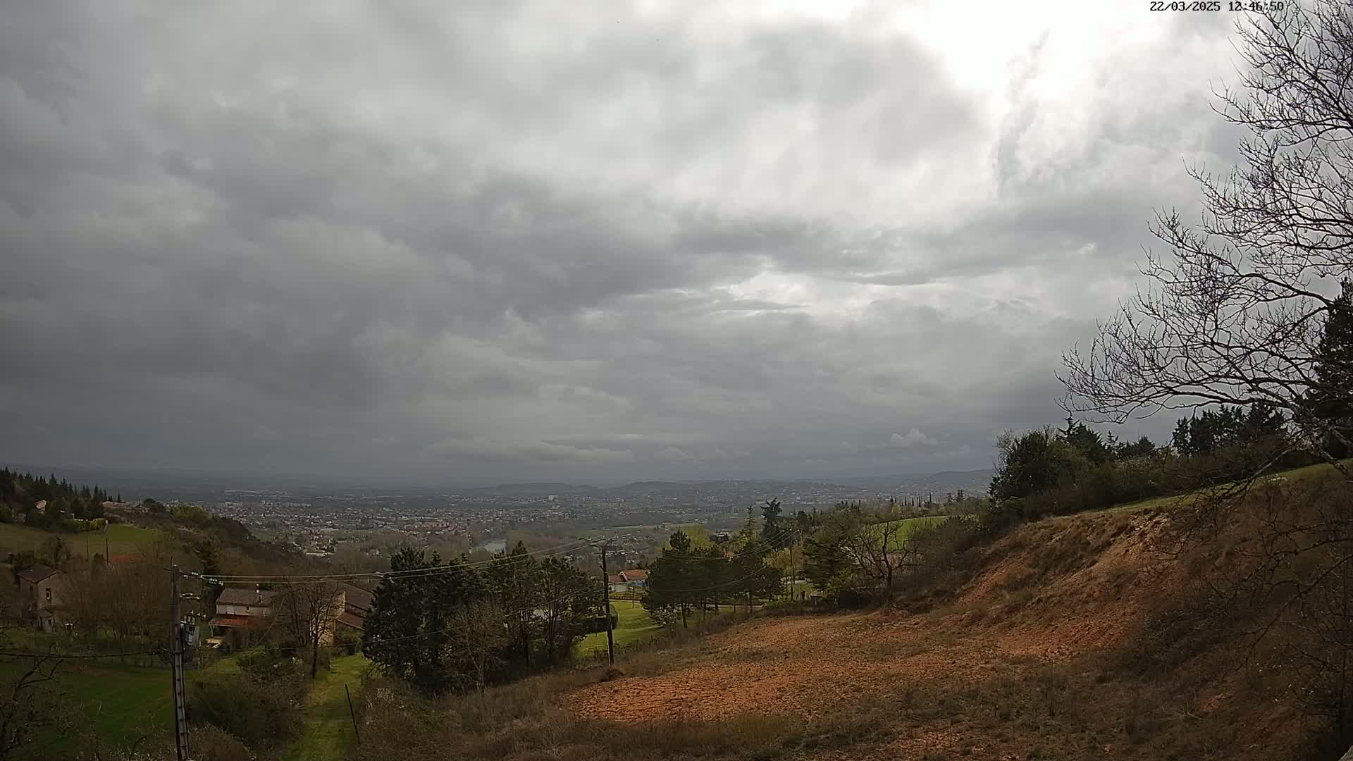 A view from a hillside shows a distant city under a heavily overcast sky.
