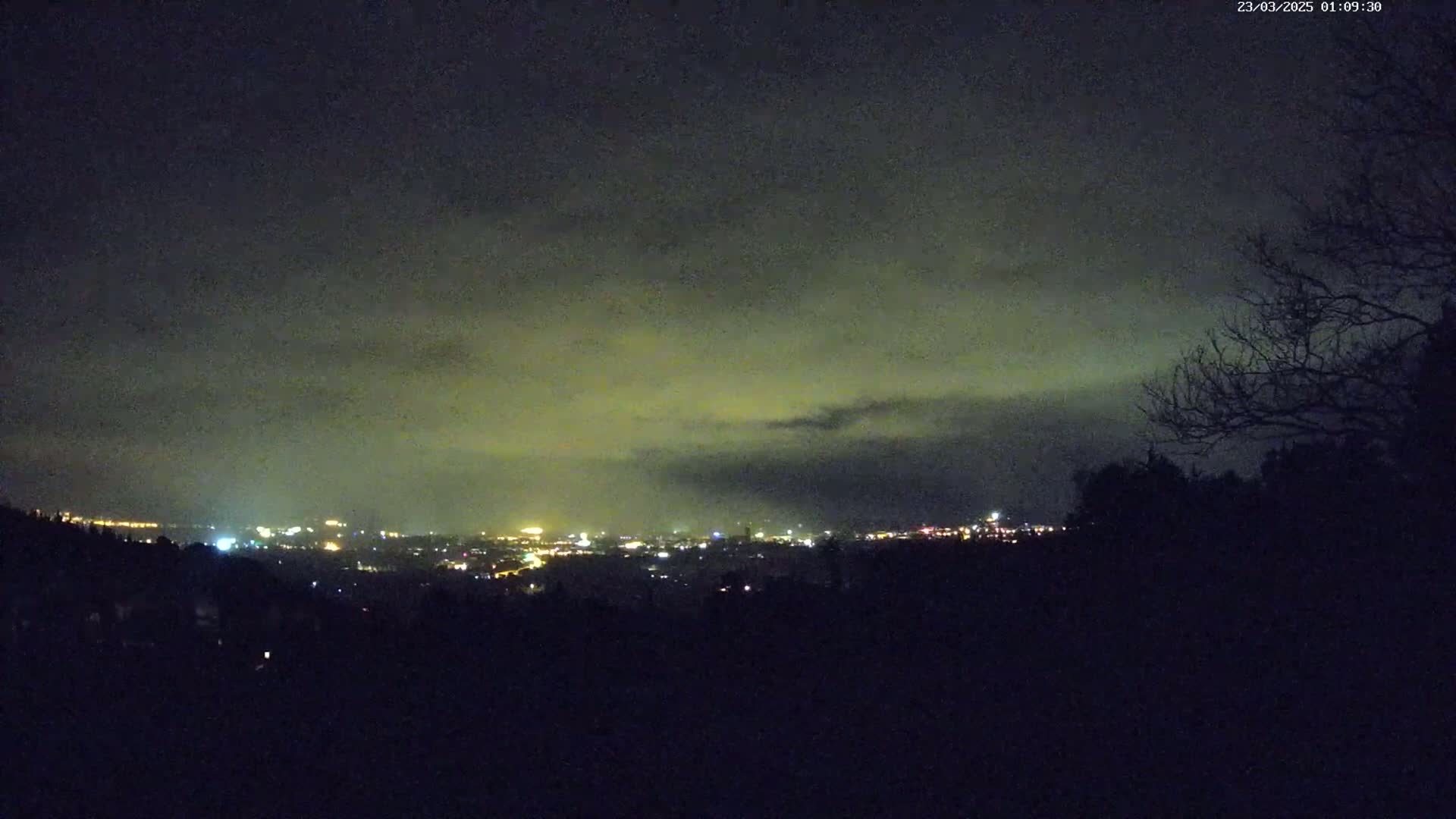 A nighttime view of a distant city glowing under a cloudy sky.