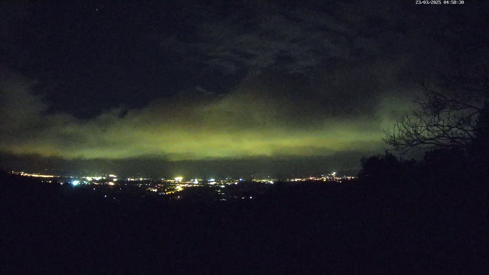 A nighttime view of a city's lights under a clouded, greenish sky.