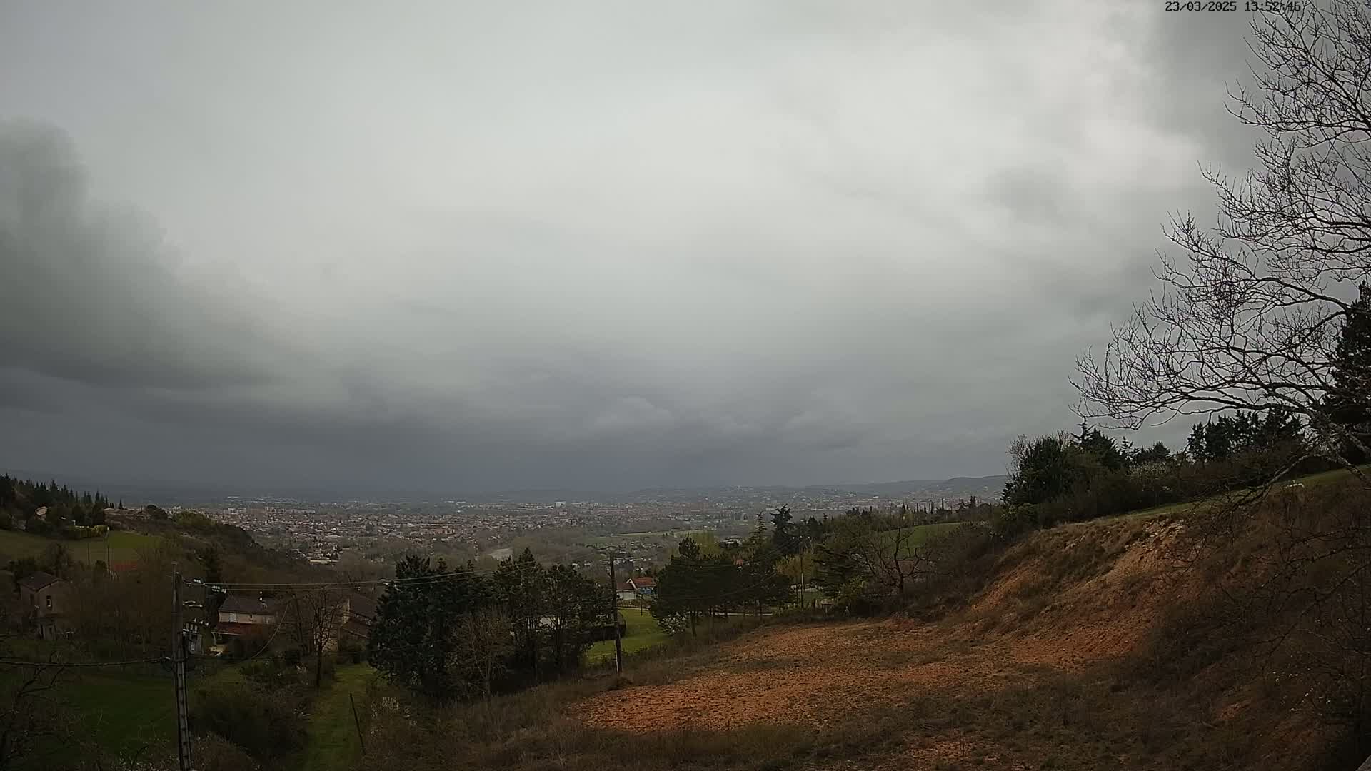A hilly landscape under an overcast sky shows a distant city spread out below.