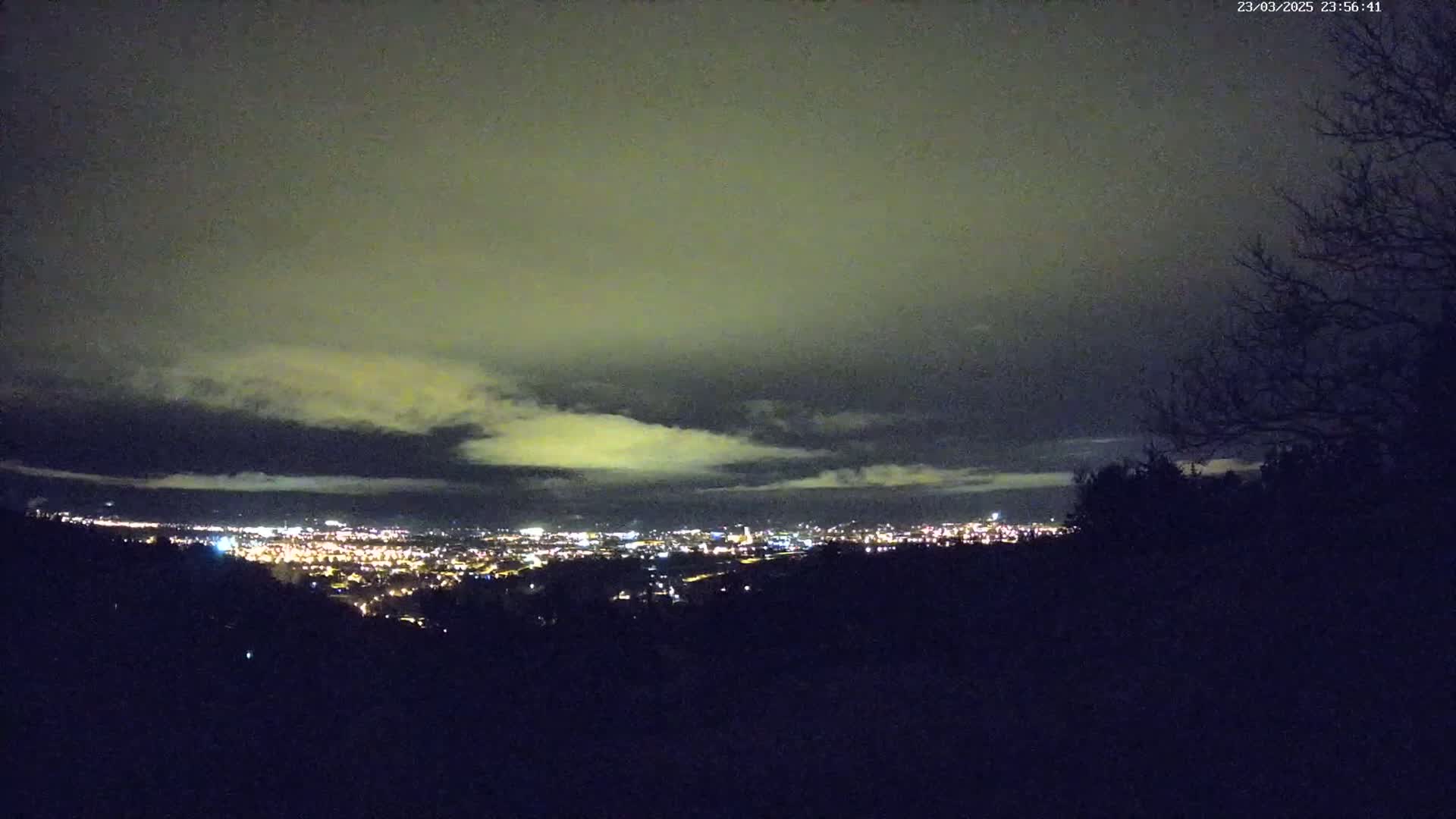 A nighttime view from a hilltop shows a city illuminated below a cloudy sky.