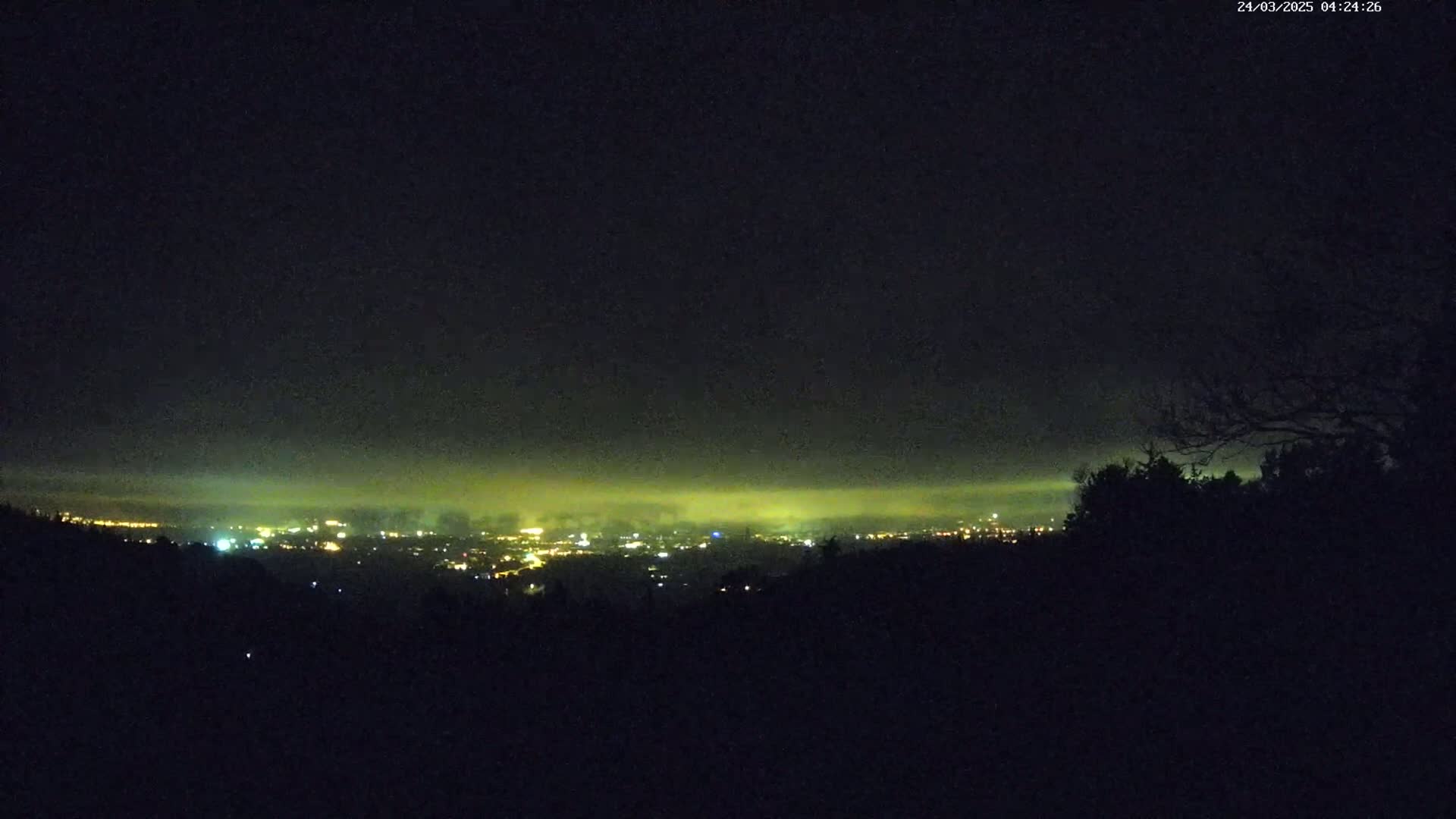 A nighttime view from an elevated position shows a distant city glowing faintly under a hazy, dark sky.