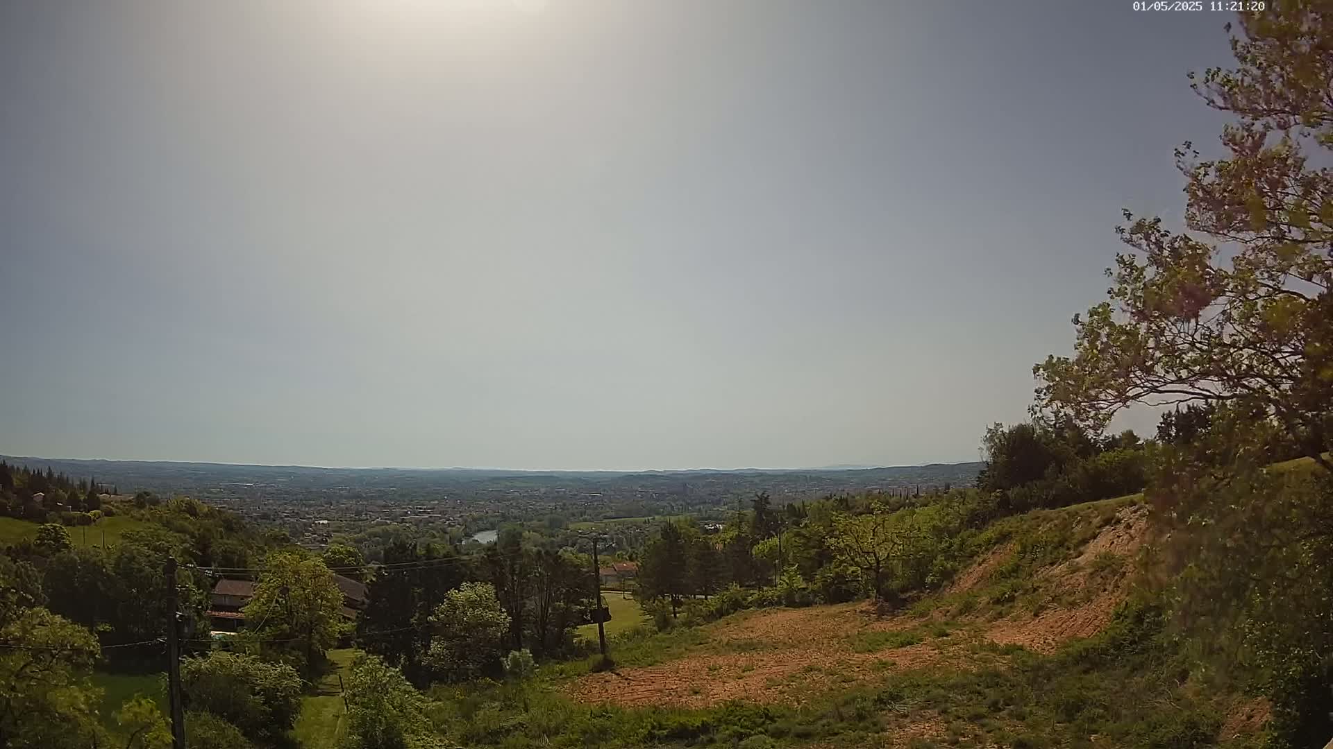 A sunny day reveals a hilly landscape with lush green vegetation, overlooking a distant city sprawling across a valley.