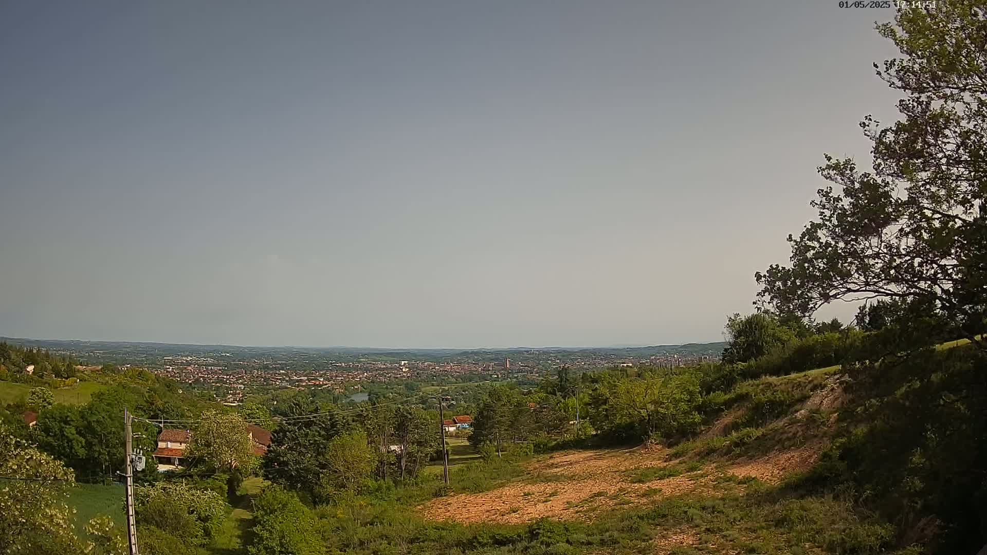 A hilly landscape with lush green trees and a distant view of a city under a hazy sky.