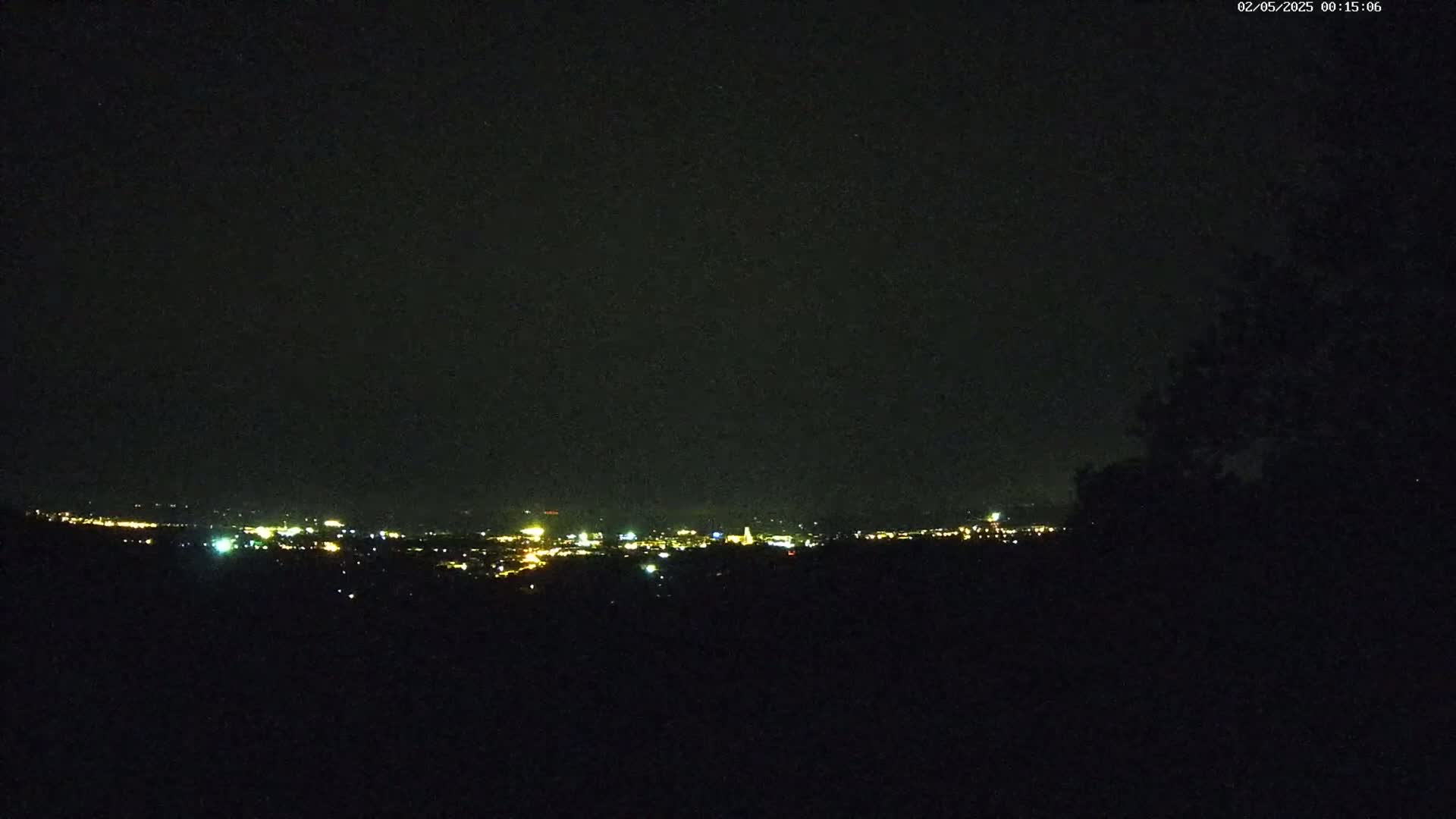 A distant city skyline is faintly visible at night from a dark, elevated vantage point.