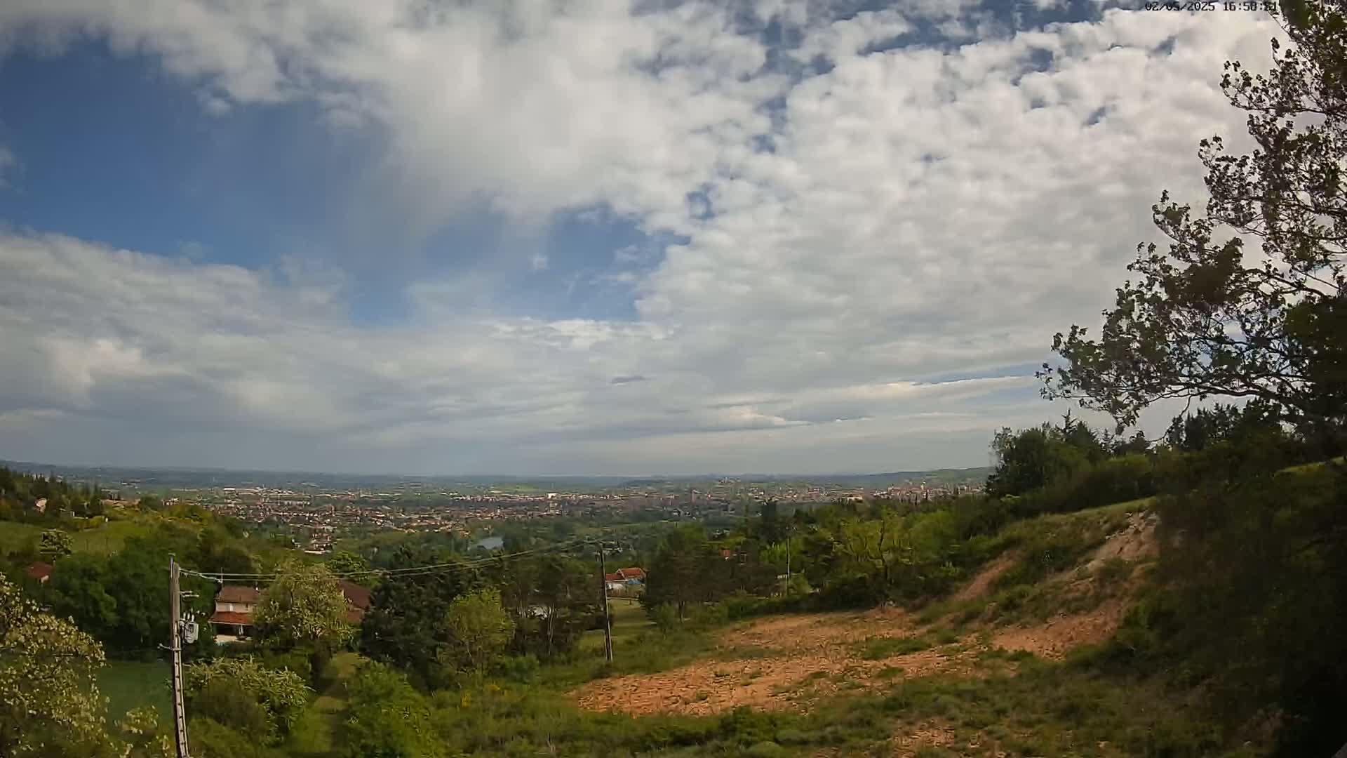 A partly cloudy sky overlooks a sprawling town nestled in a valley of green hills and trees.