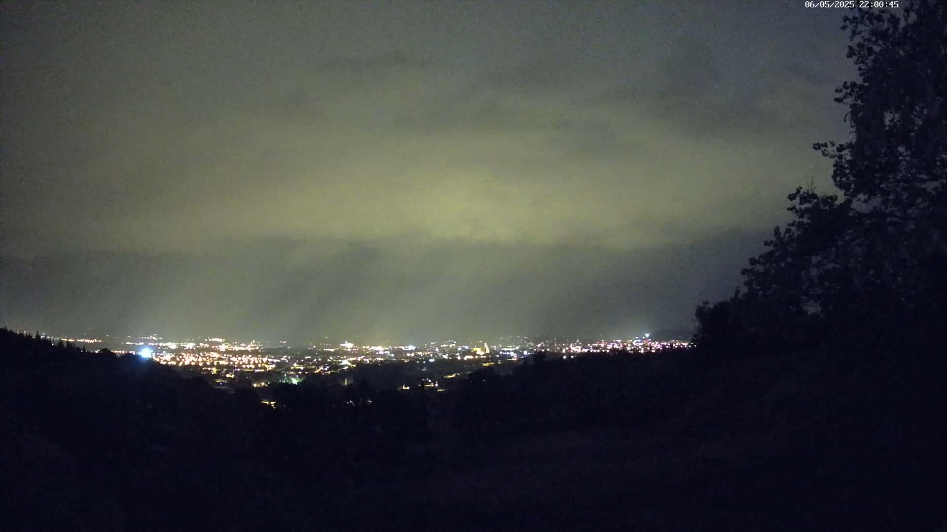 A nighttime view of a city's lights spread across a valley, under a cloudy sky.