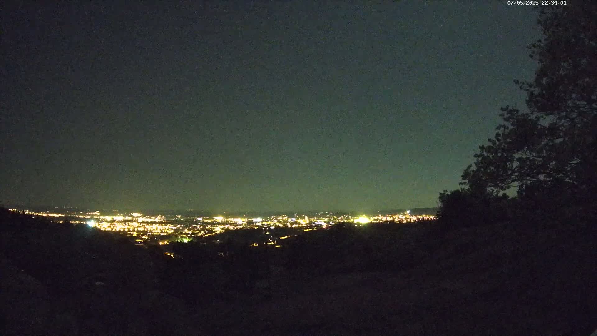 A nighttime view from an elevated vantage point shows a distant city illuminated by lights under a dark, clear sky.