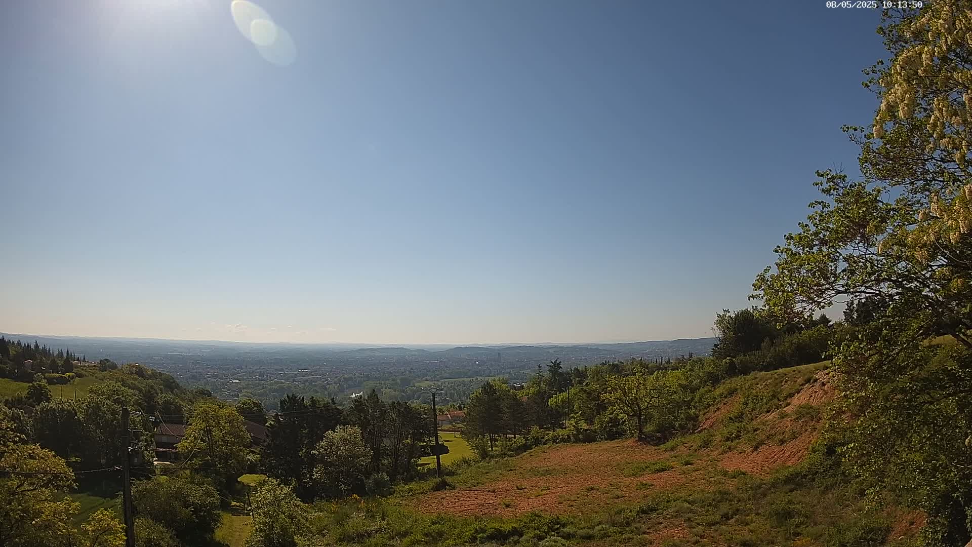 A sunny, clear day reveals a panoramic view of a sprawling city nestled in a valley, surrounded by lush green hills and trees.