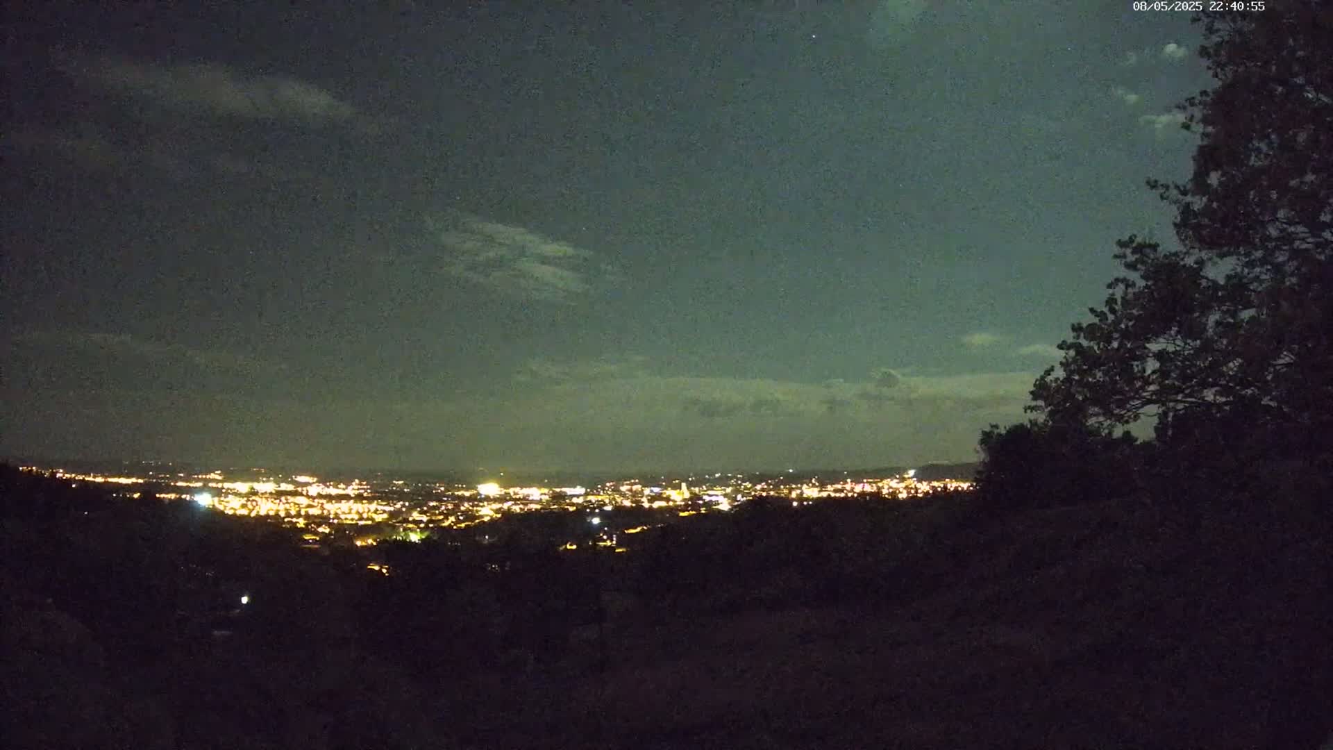 A nighttime view of a distant city illuminated by lights under a partly cloudy sky.