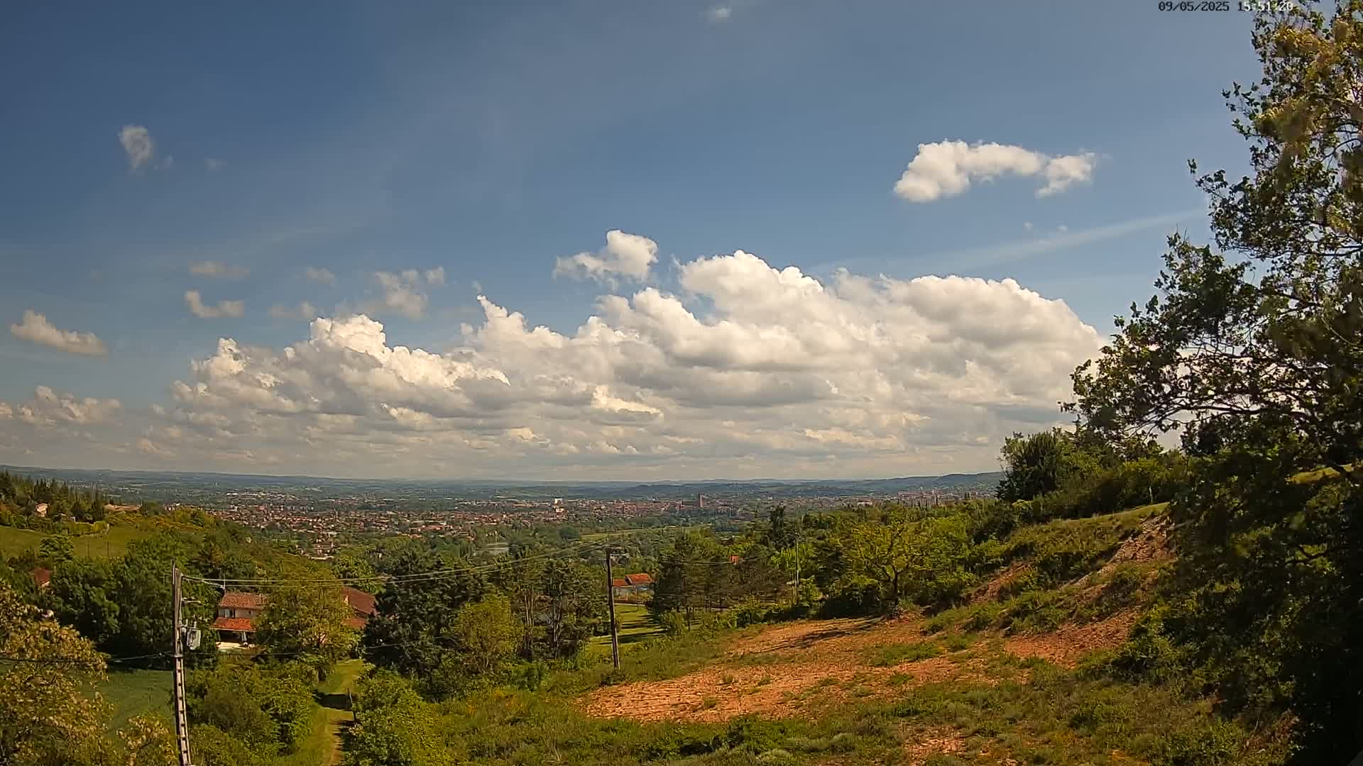 A hilly landscape with lush green trees and a distant city under a partly cloudy sky.