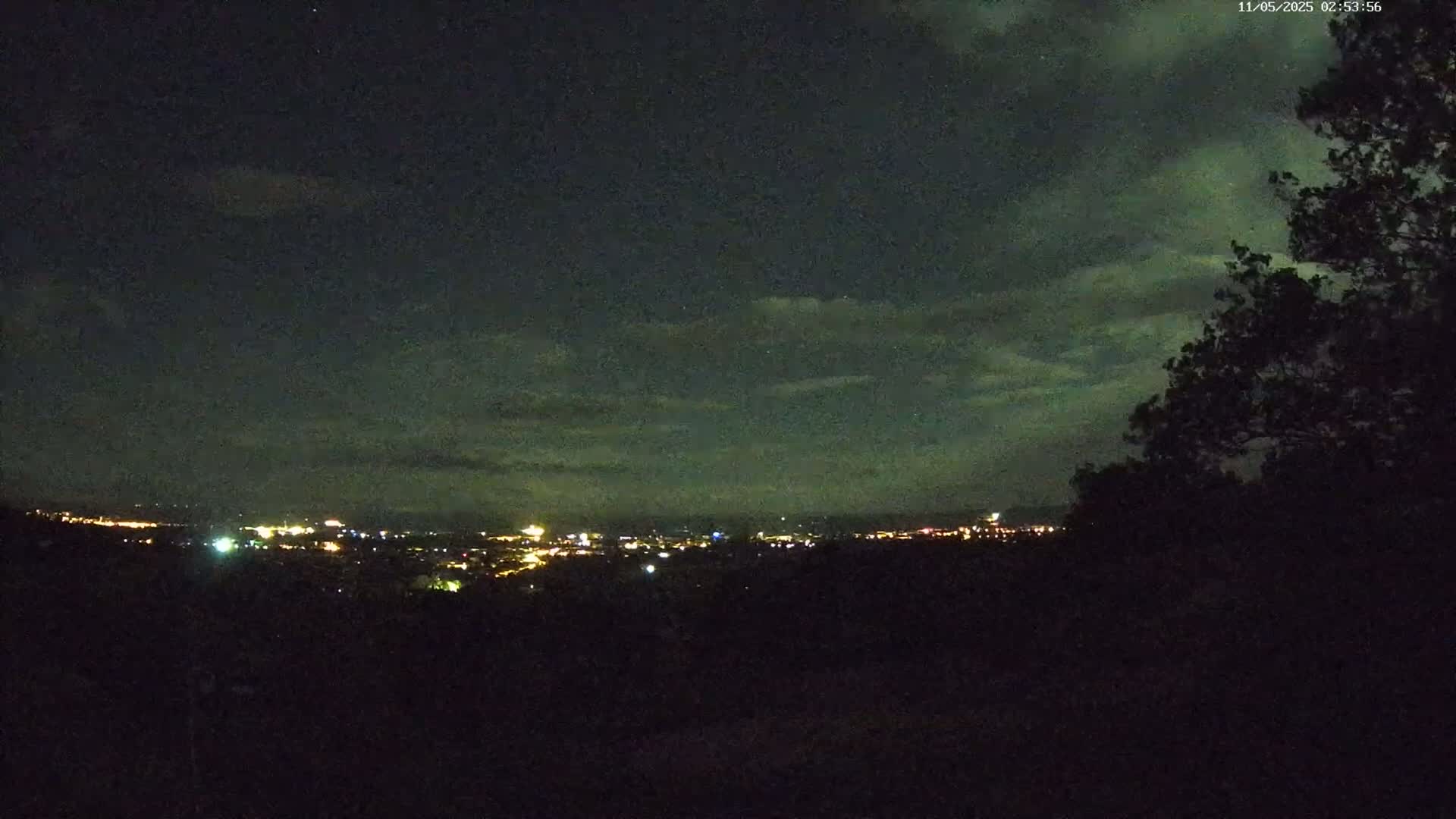 A nighttime view of a city skyline illuminated by lights under a partly cloudy sky.