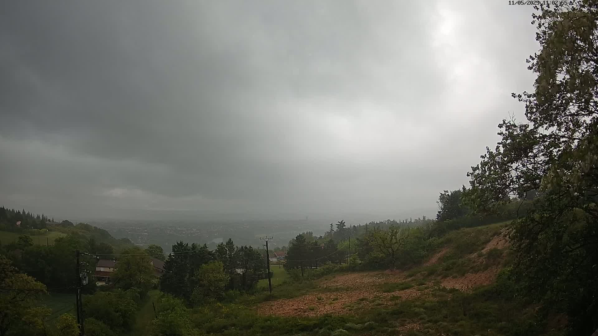 A hilly landscape with green trees and houses is visible under a heavily overcast sky.