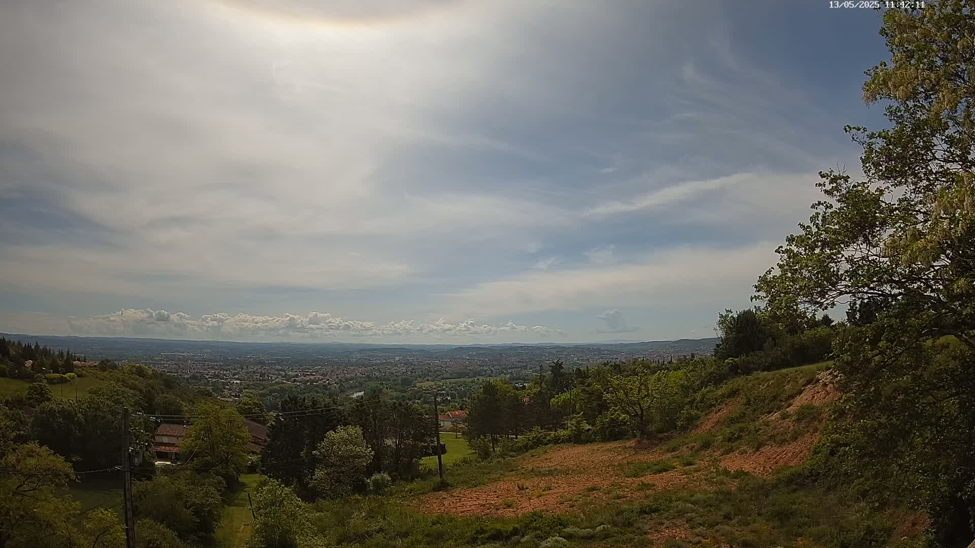 A hilly landscape with green trees and a distant city under a partly cloudy sky.