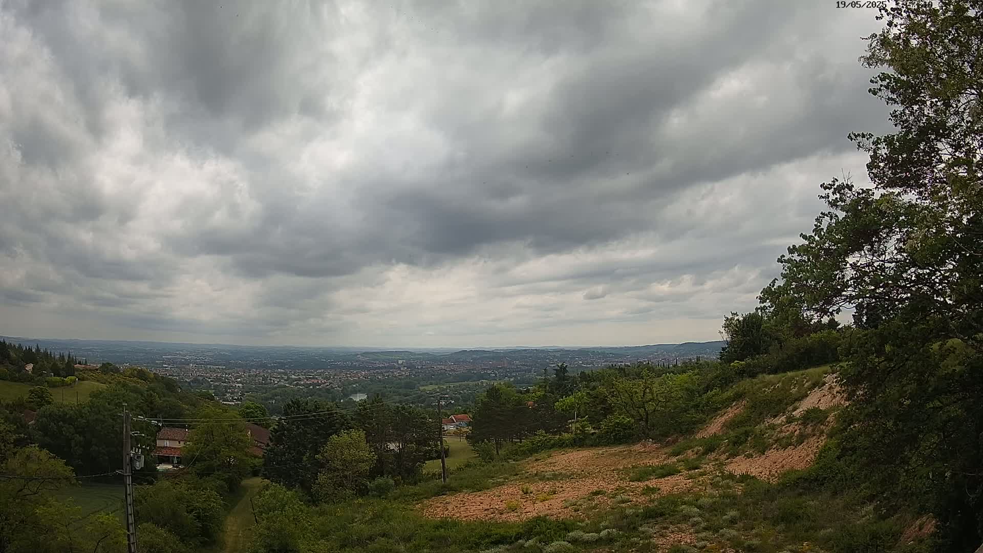 A hilly landscape with overcast skies shows a distant city sprawling beneath a grey sky.
