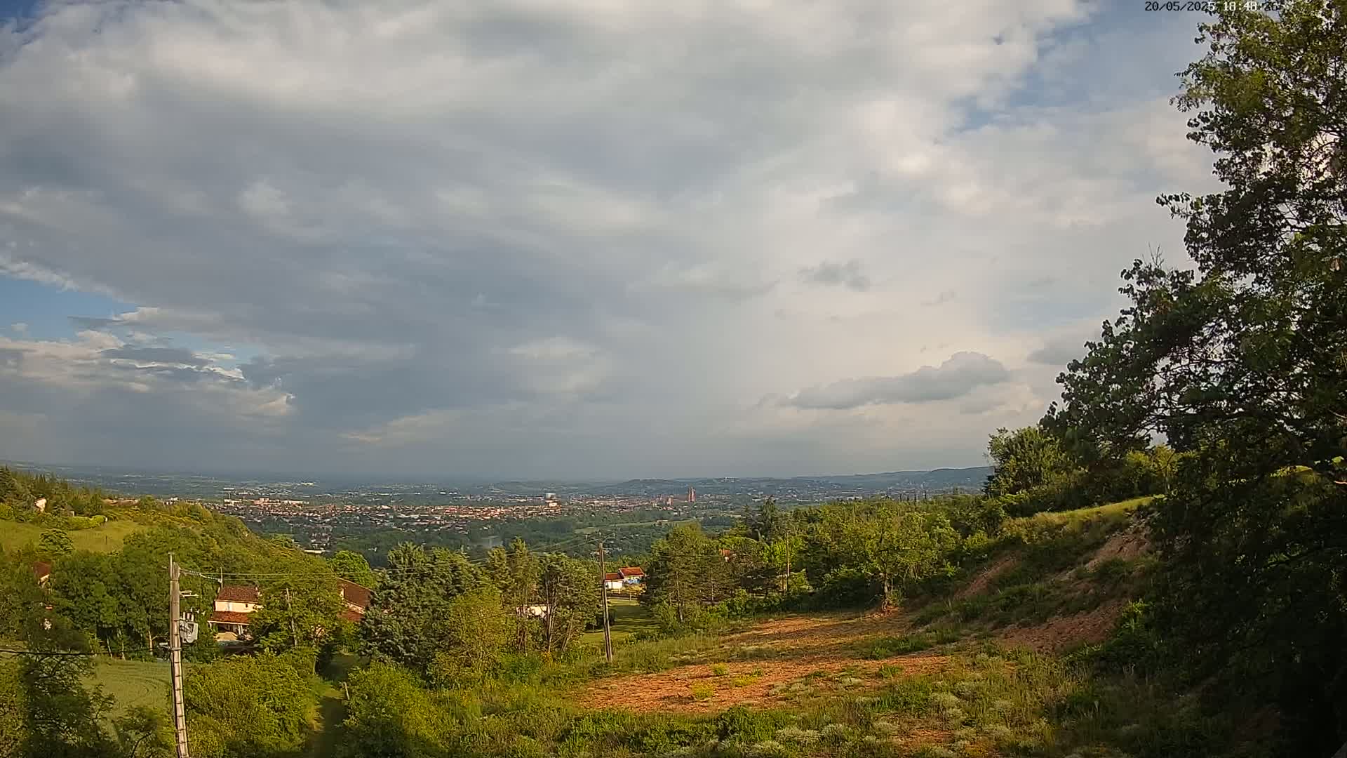 A hilly landscape with lush green trees and vegetation overlooks a distant city under a partly cloudy sky.