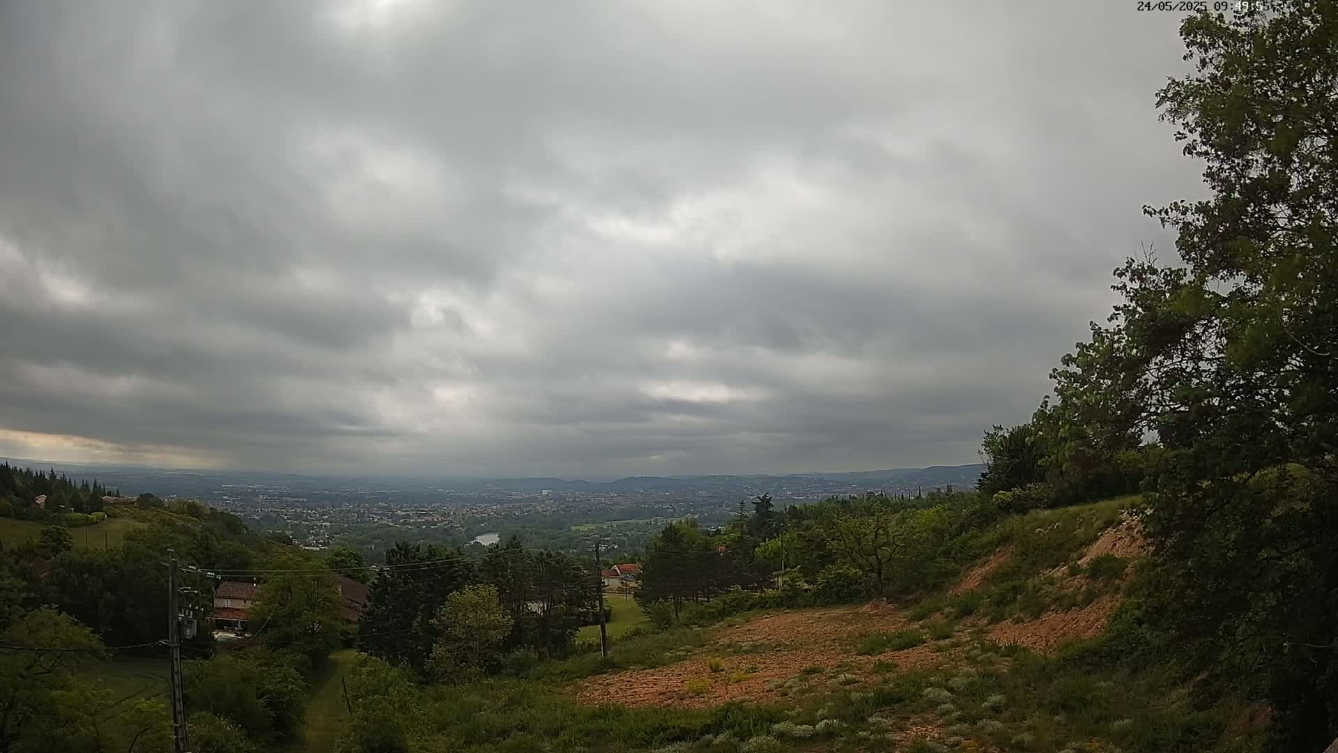 A hilly, green landscape with overcast skies overlooks a distant city.