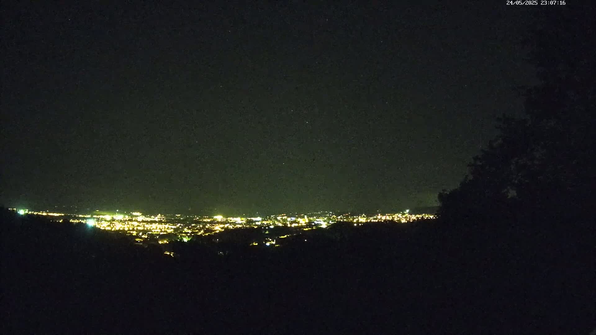 A nighttime view from a hilltop shows a distant city illuminated by lights under a clear, dark sky.