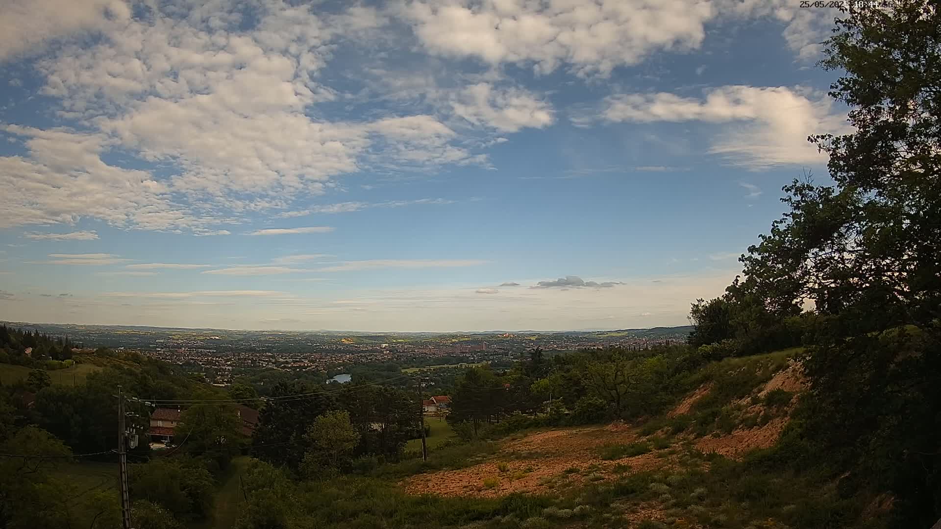 A hilly landscape with a view of a distant city under a partly cloudy sky.