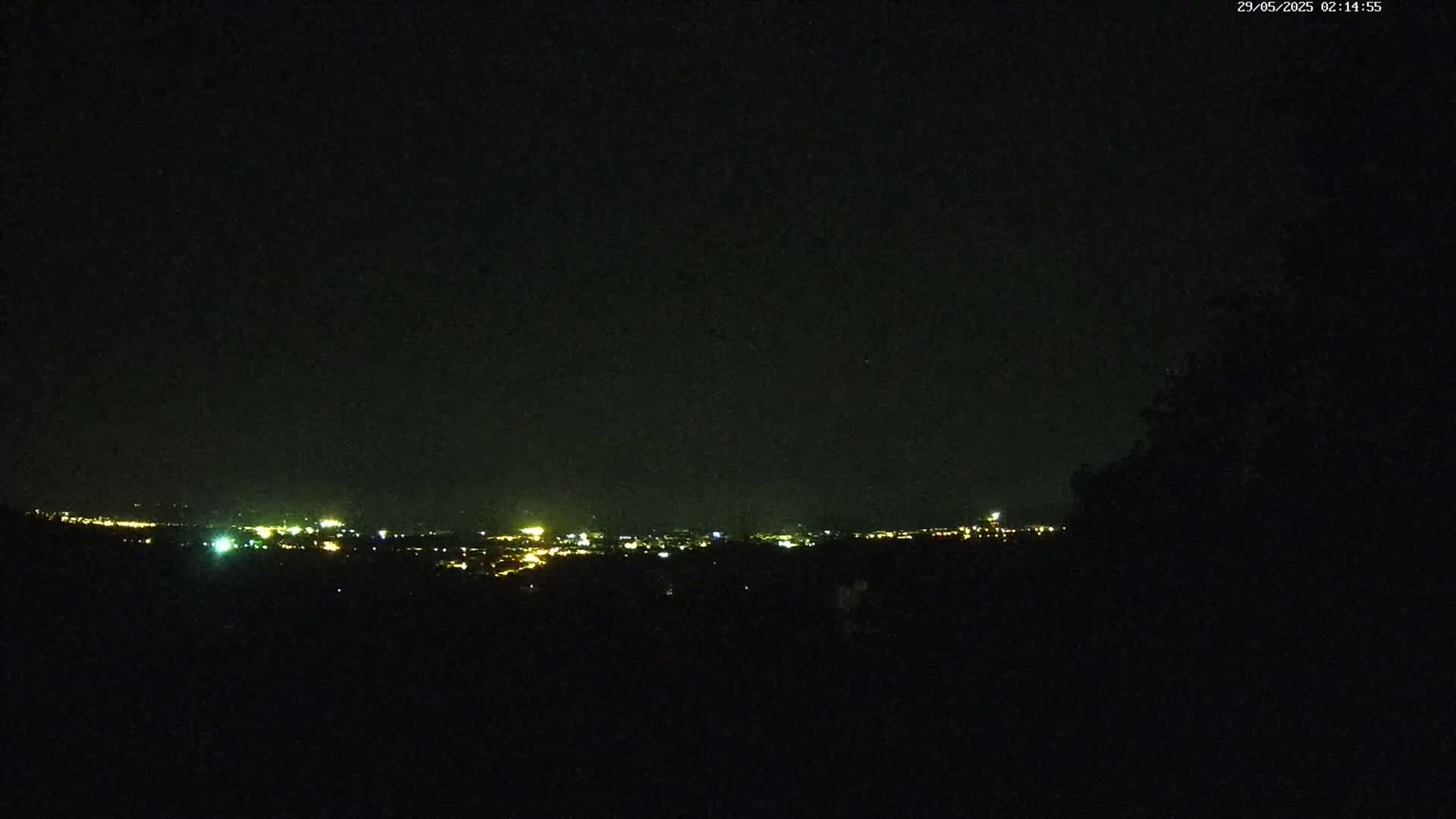 A distant city's lights are visible on the horizon at night from a dark, elevated vantage point.